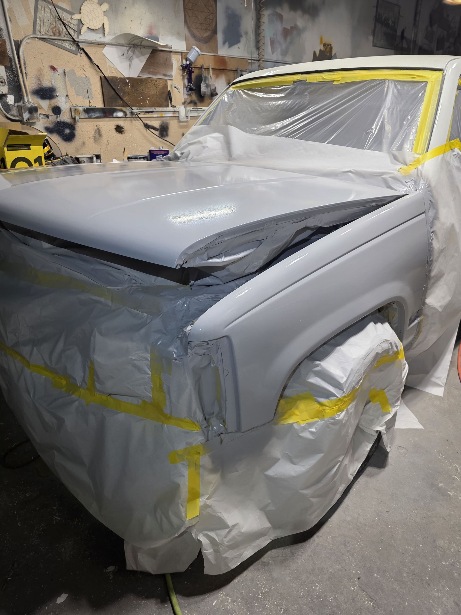 Partially covered car with gray primer and yellow masking tape in a workshop