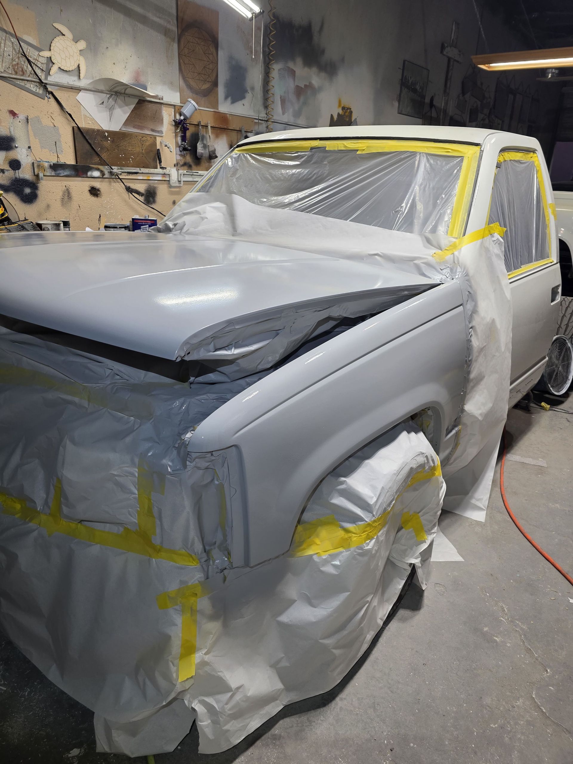 Car covered with primer and masking tape in a body shop, with a damaged front end.
