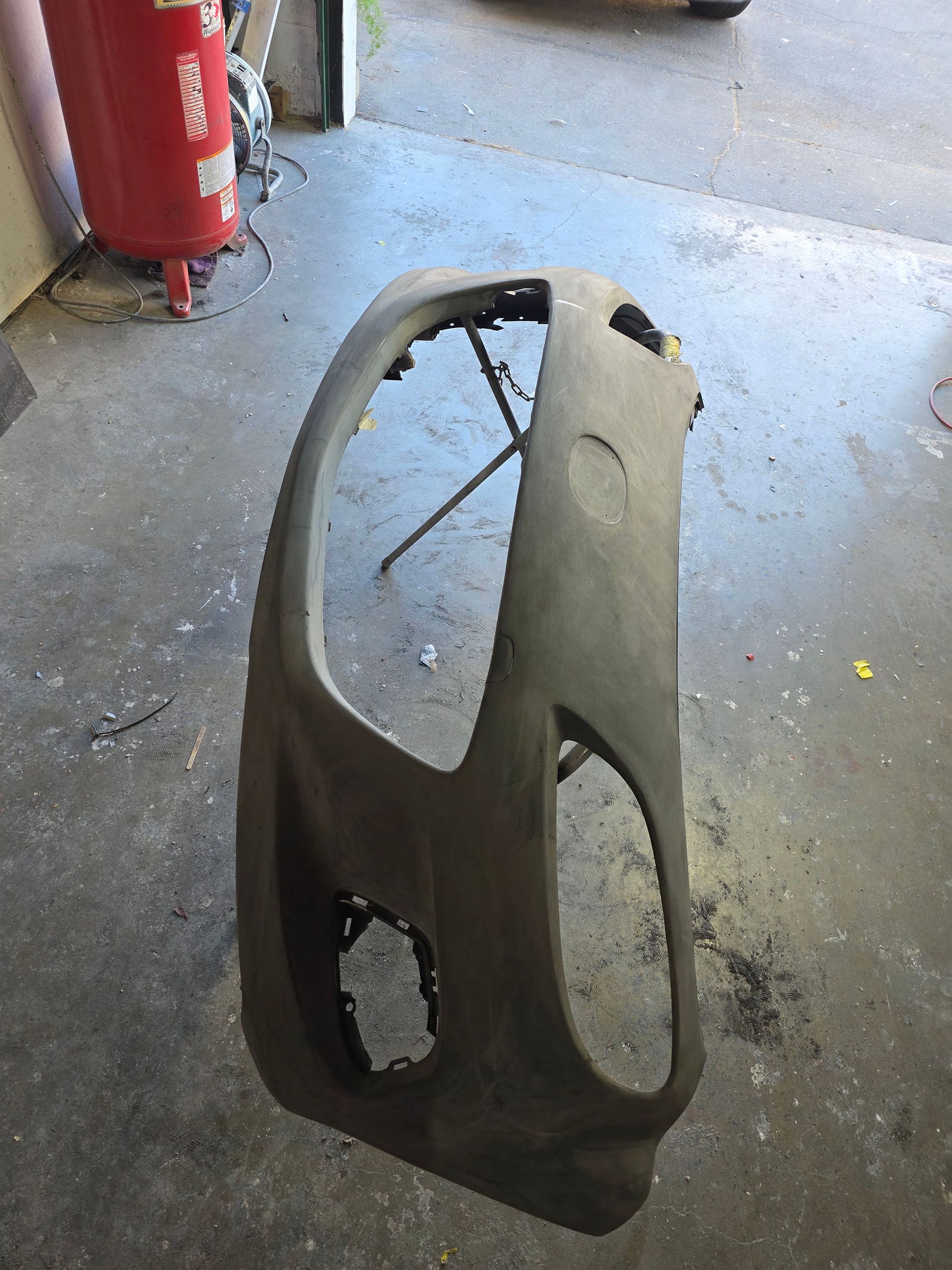 Damaged gray car bumper cover on a workshop floor near a red fire extinguisher.