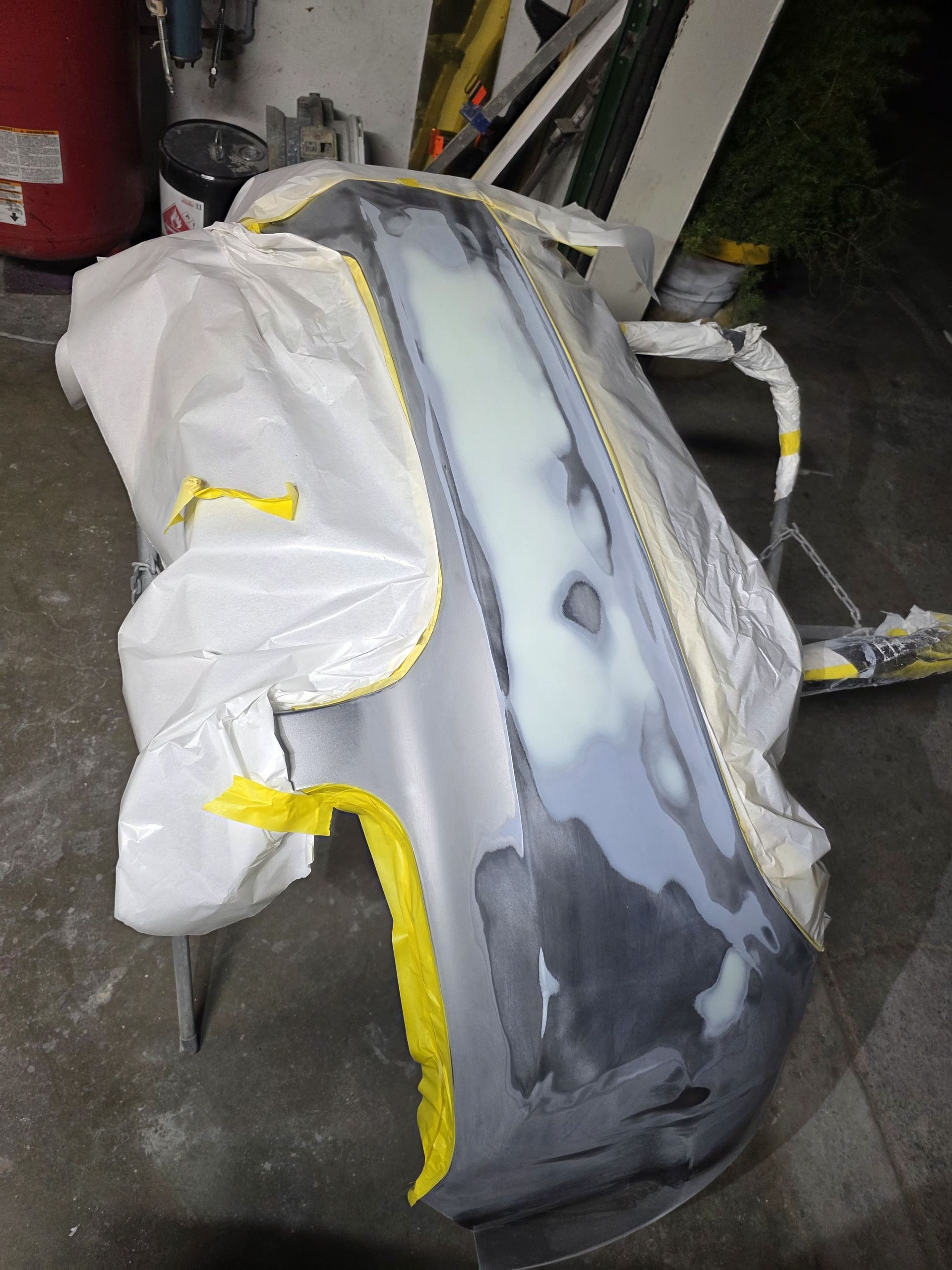 Partially masked car body with gray primer and white/yellow masking tape in a workshop