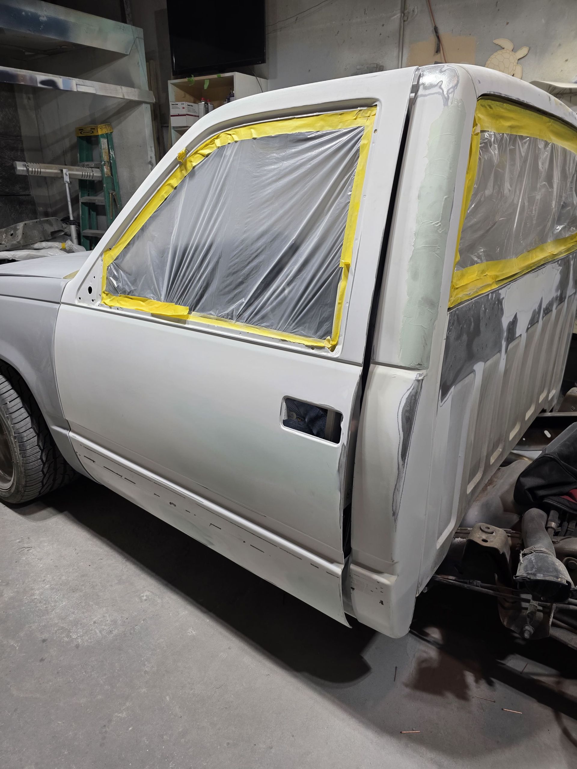 White pickup truck cab in a workshop, with windows taped off for painting or repair.
