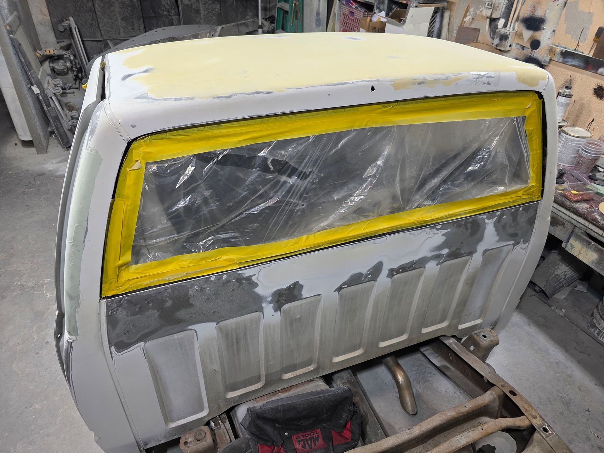 Gray vehicle body panel masked with yellow tape and plastic in a workshop for painting