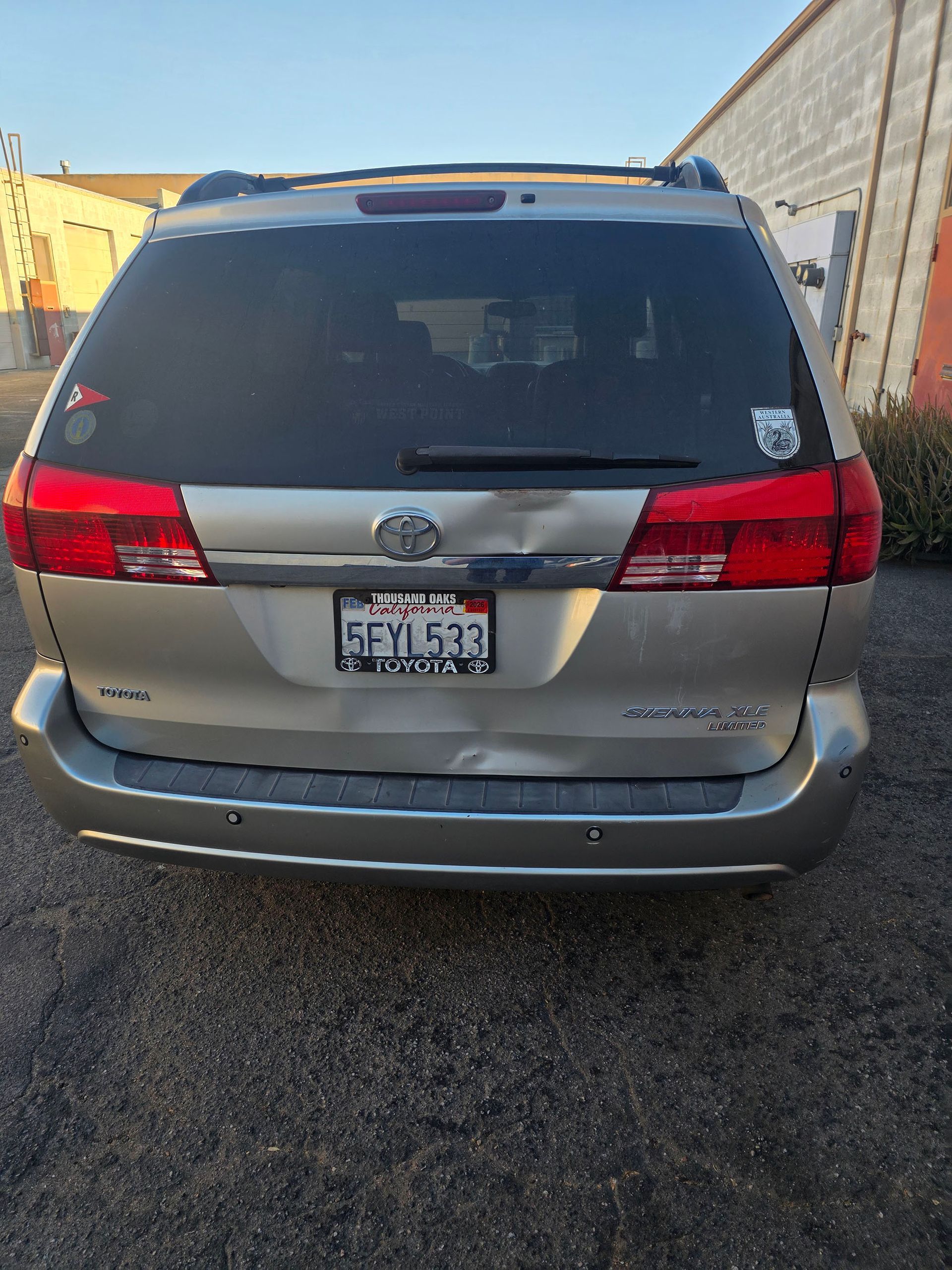 Rear view of a silver Toyota minivan parked in a narrow gravel alley.
