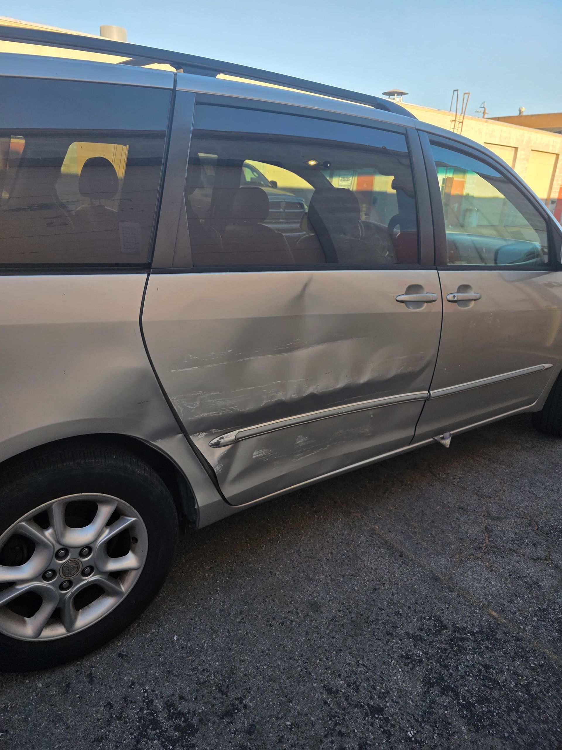 Silver minivan with a dented side panel parked on asphalt in daylight