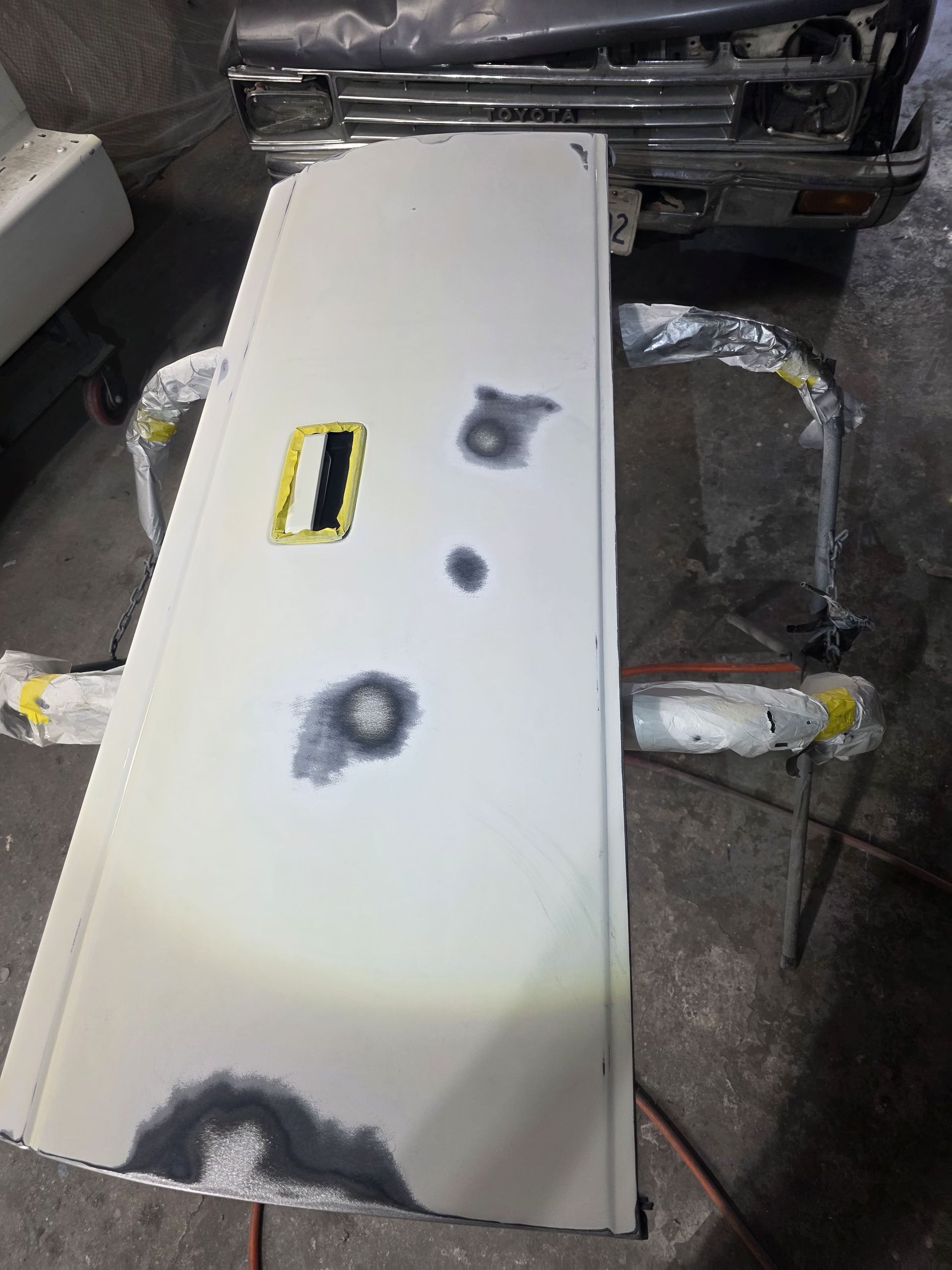 White car door panel with paint repair patches and a yellow handle opening, leaning against another vehicle.
