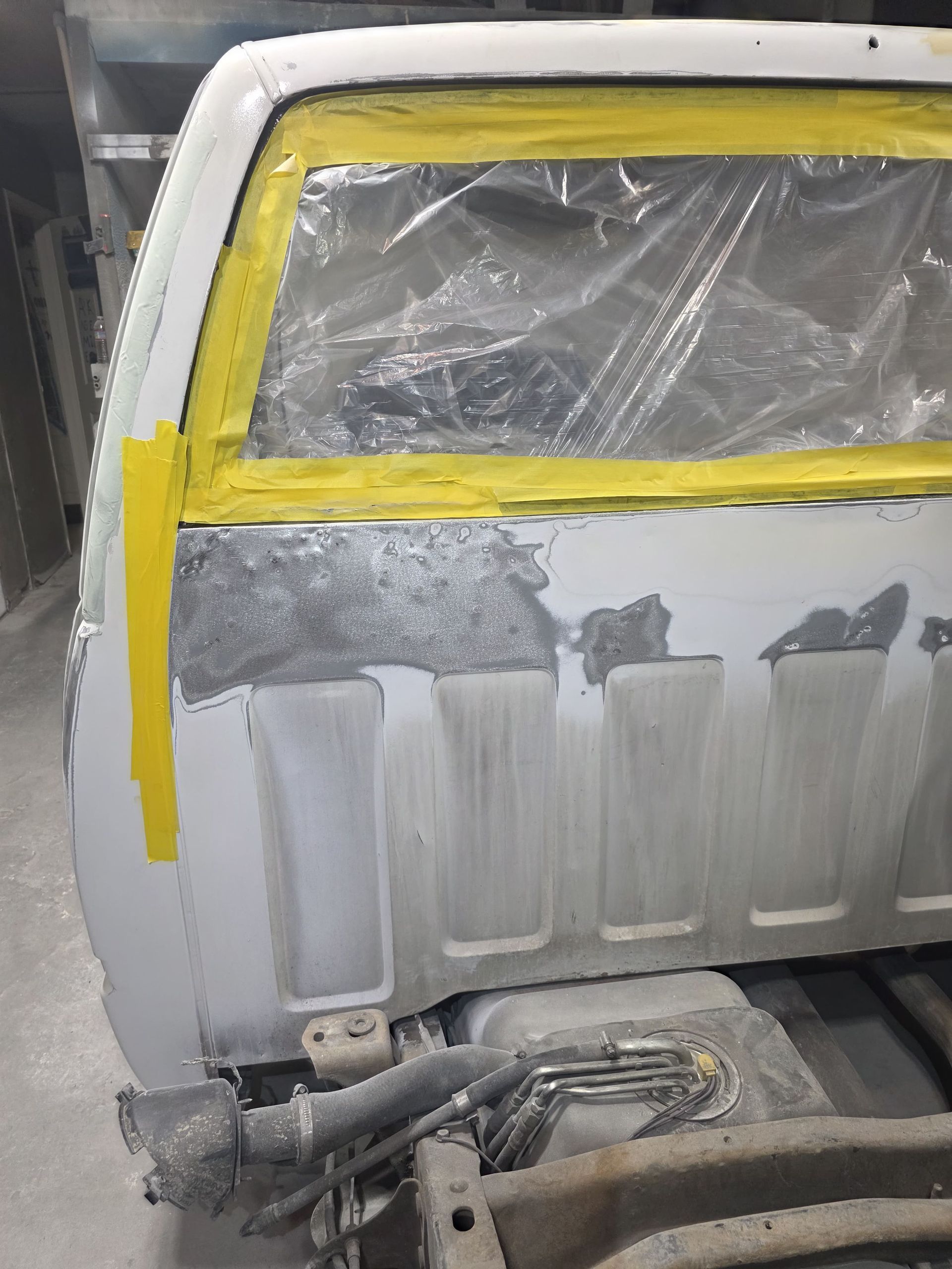 Masked silver vehicle body panel with yellow tape and plastic covering, showing repair work.