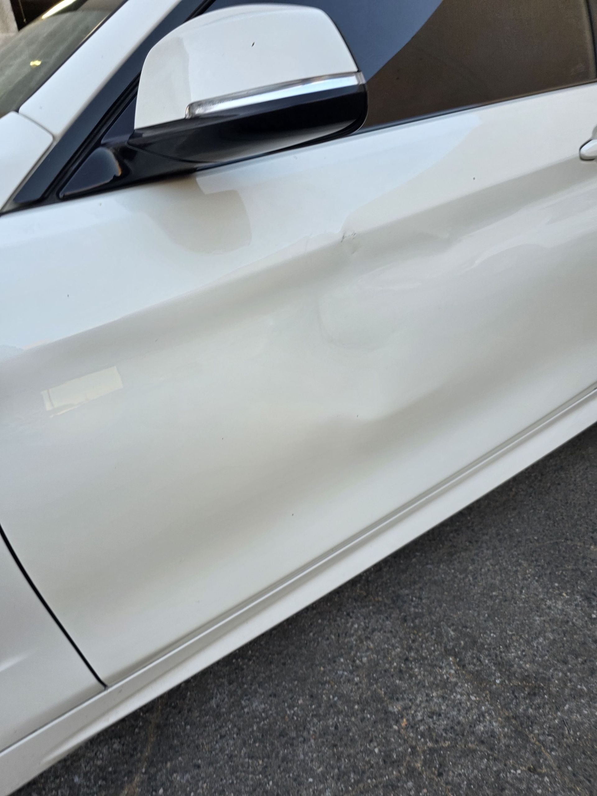 Close-up of a white car’s side door with a dent near the lower panel.
