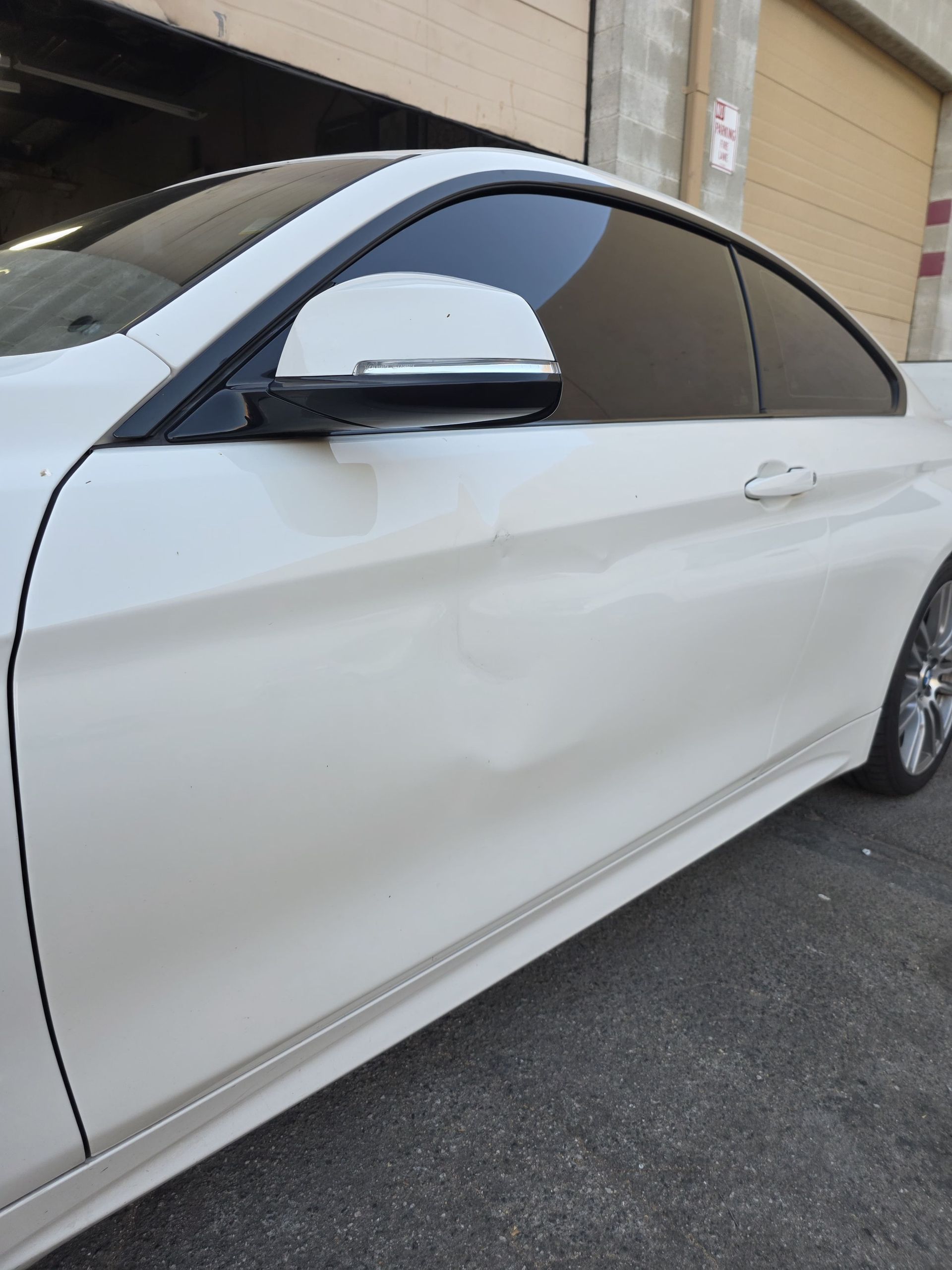 White sedan parked beside a beige building, side view with tinted windows and black side mirror