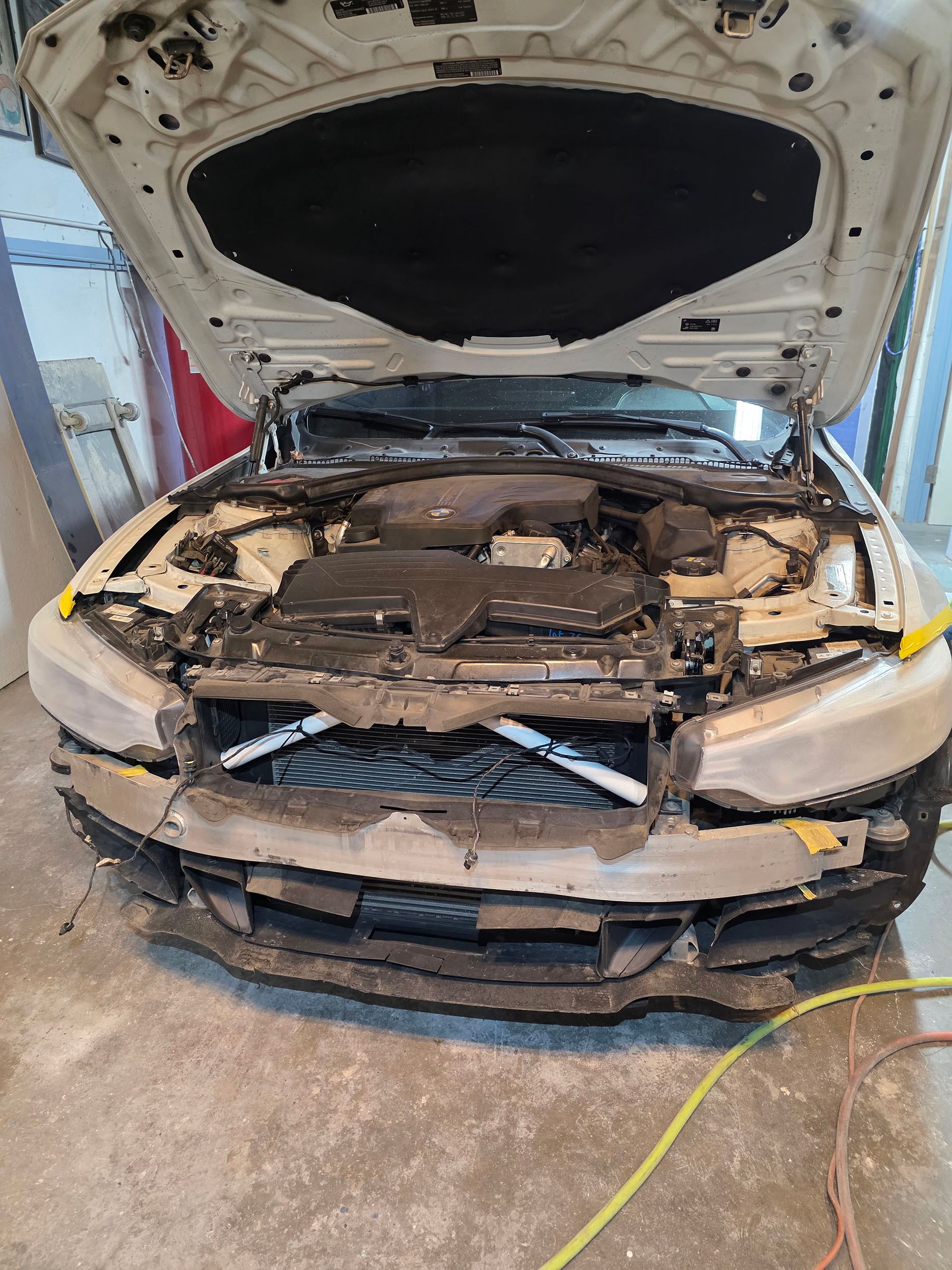 Damaged car with hood open, front bumper removed, and exposed engine in a garage