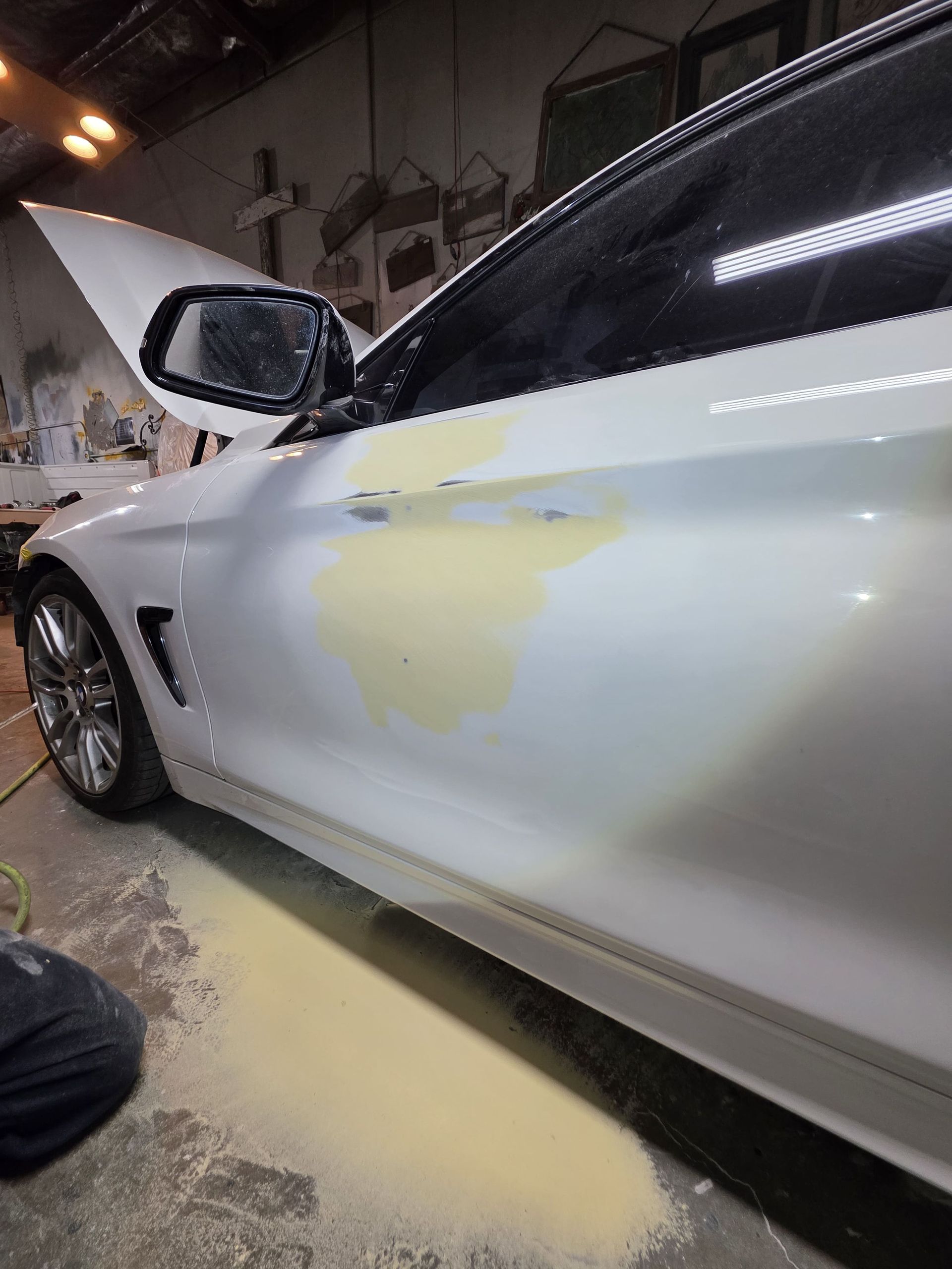 White car with yellow body filler on the side panel in a dimly lit garage at night