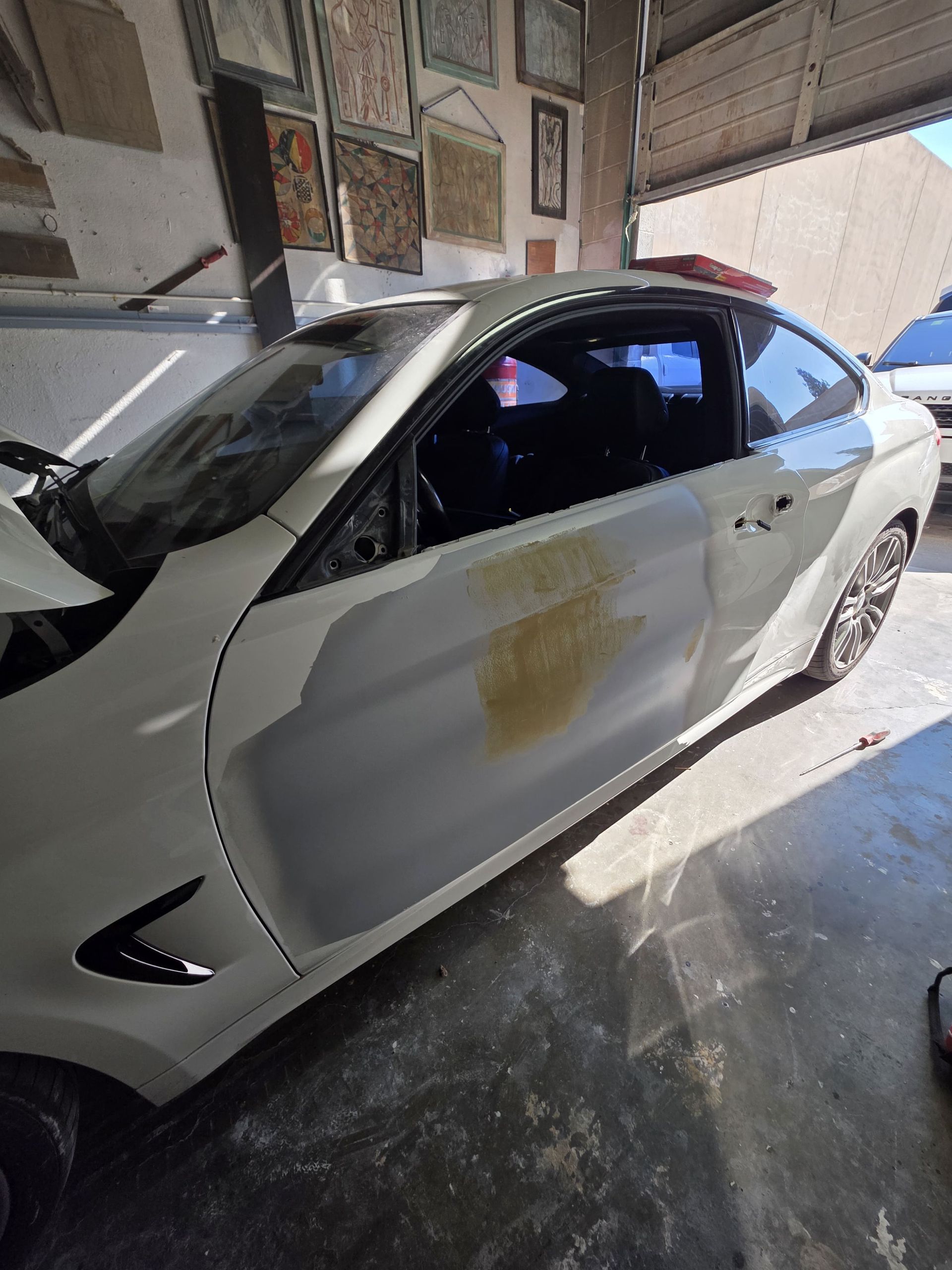 White sedan with a dented side door parked in a garage, with a repair patch on the door panel