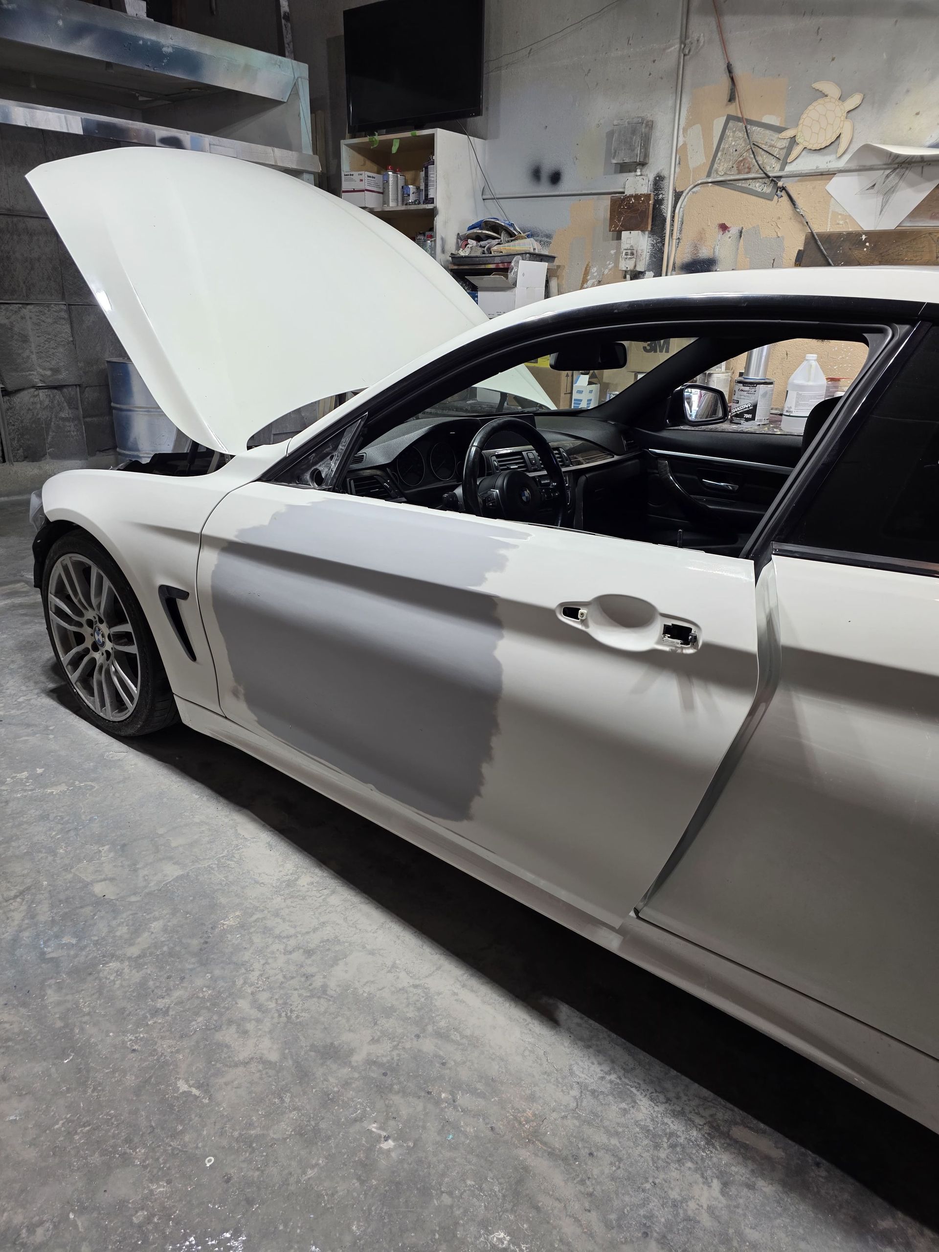 White car with hood open in a garage, showing body damage on the side.