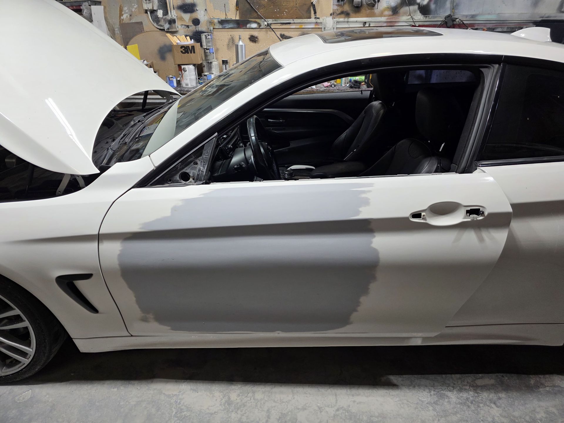 White coupe with open hood and damaged side, likely after a collision in a garage setting