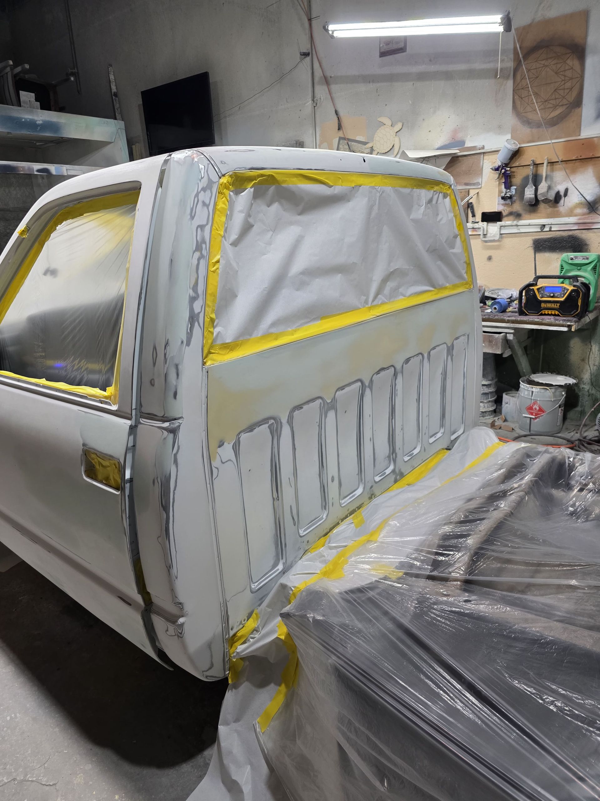Car body in a workshop, masked with tape and plastic for painting; rear and side panels primed gray.