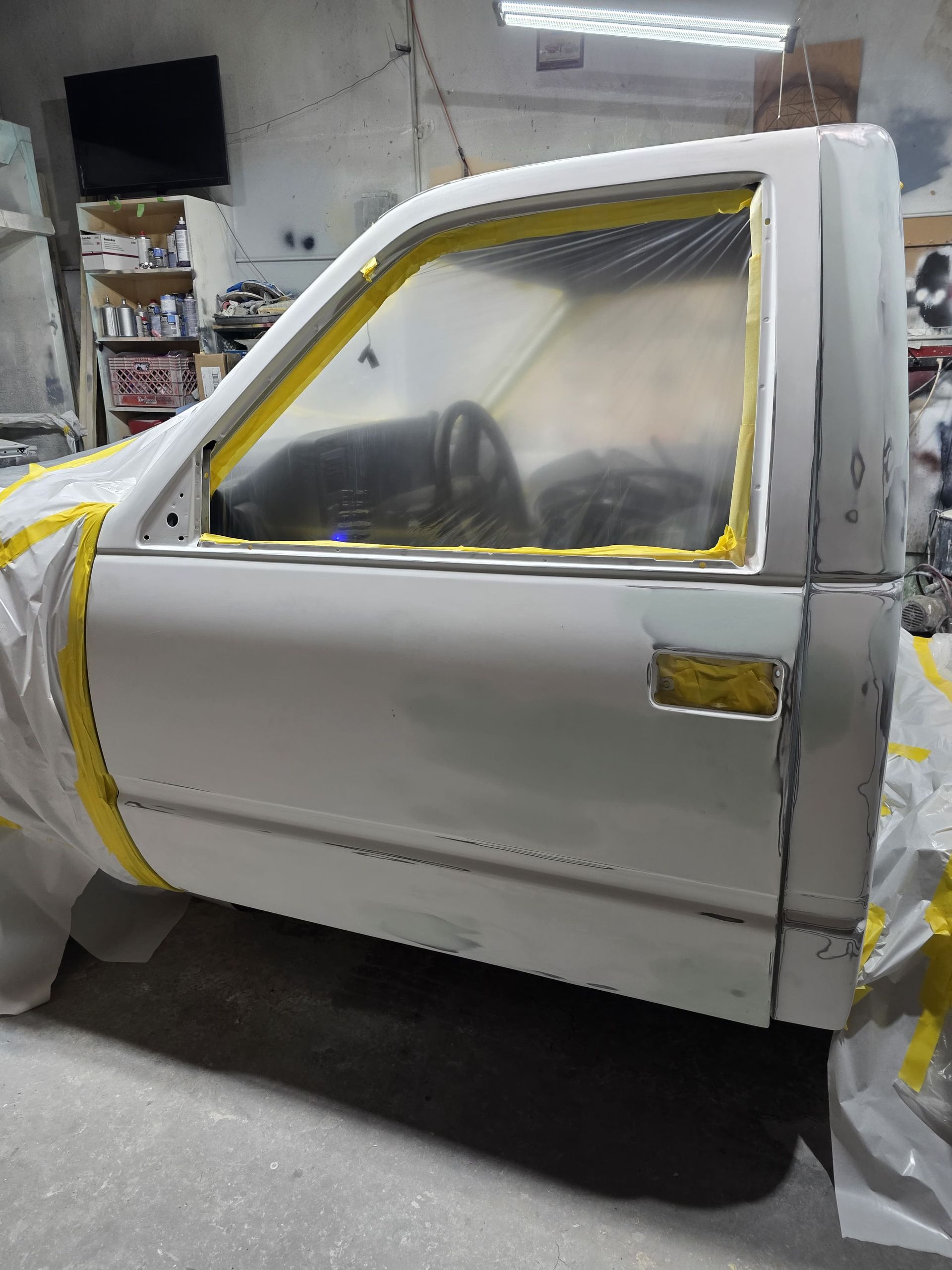 Car door and window masked with yellow tape and plastic in a paint shop, ready for spraying