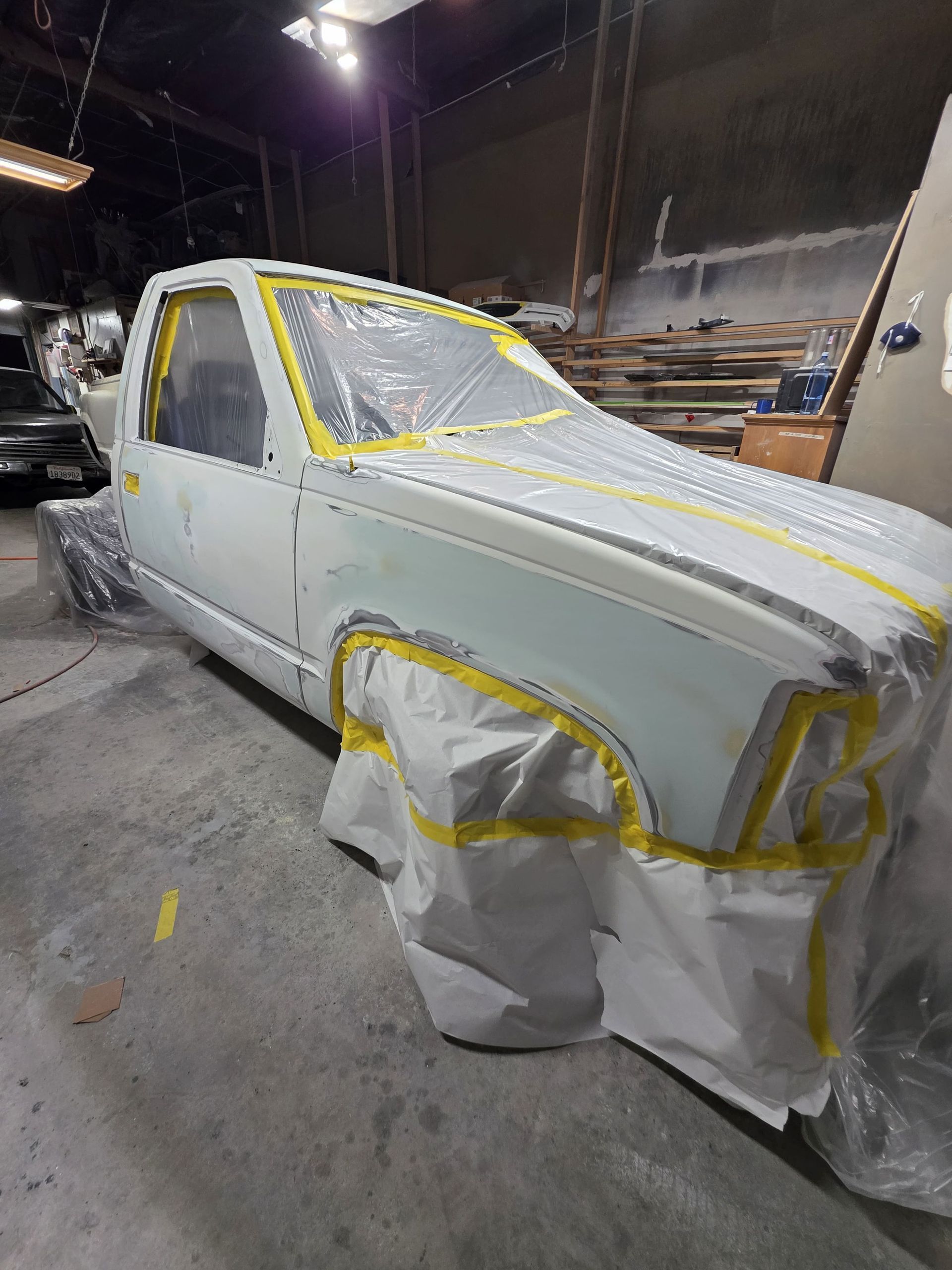 White pickup truck masked with tape and plastic in a workshop, under repair or paint prep.