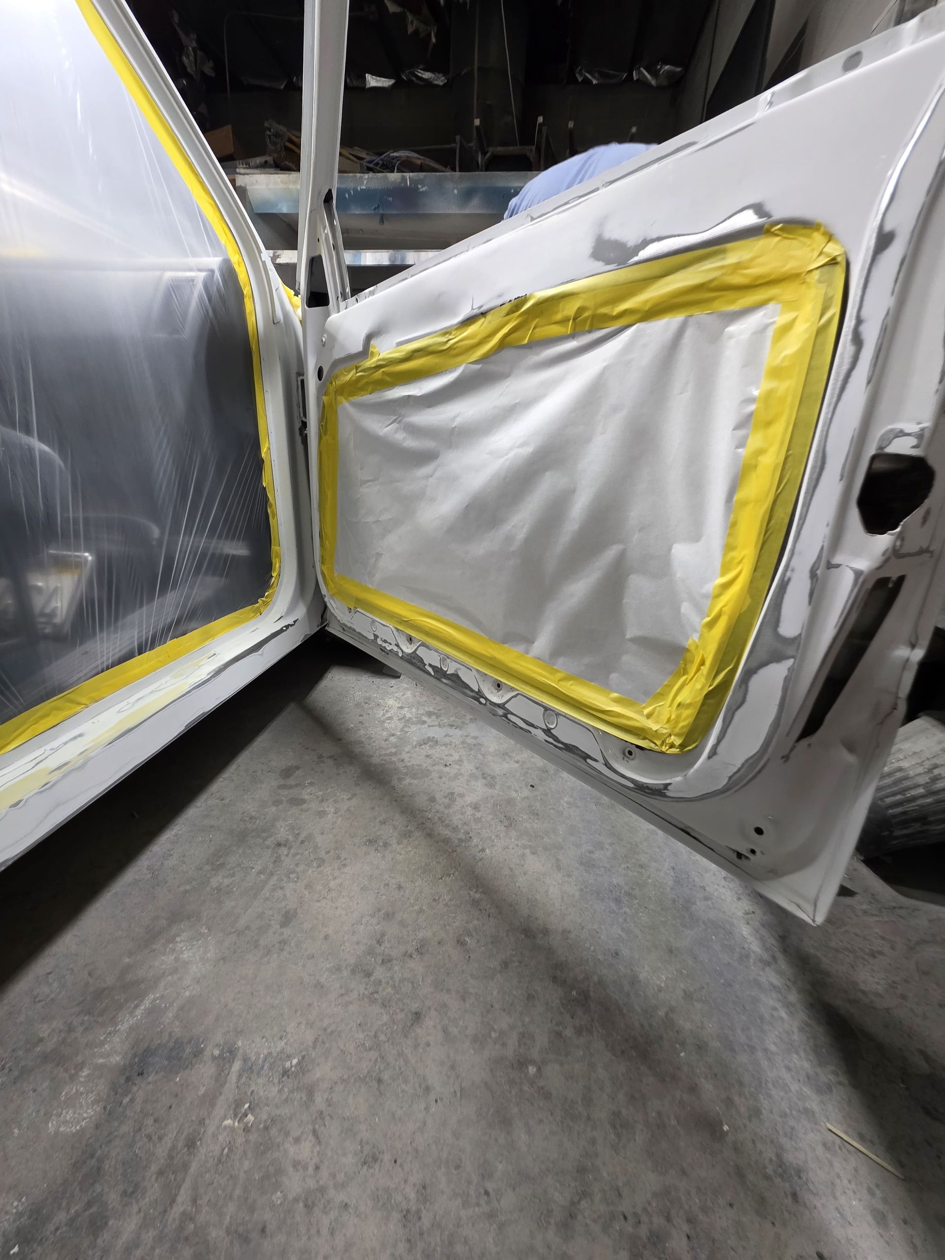 Two car doors open, showing silver interior panels with yellow tape and a concrete floor below.