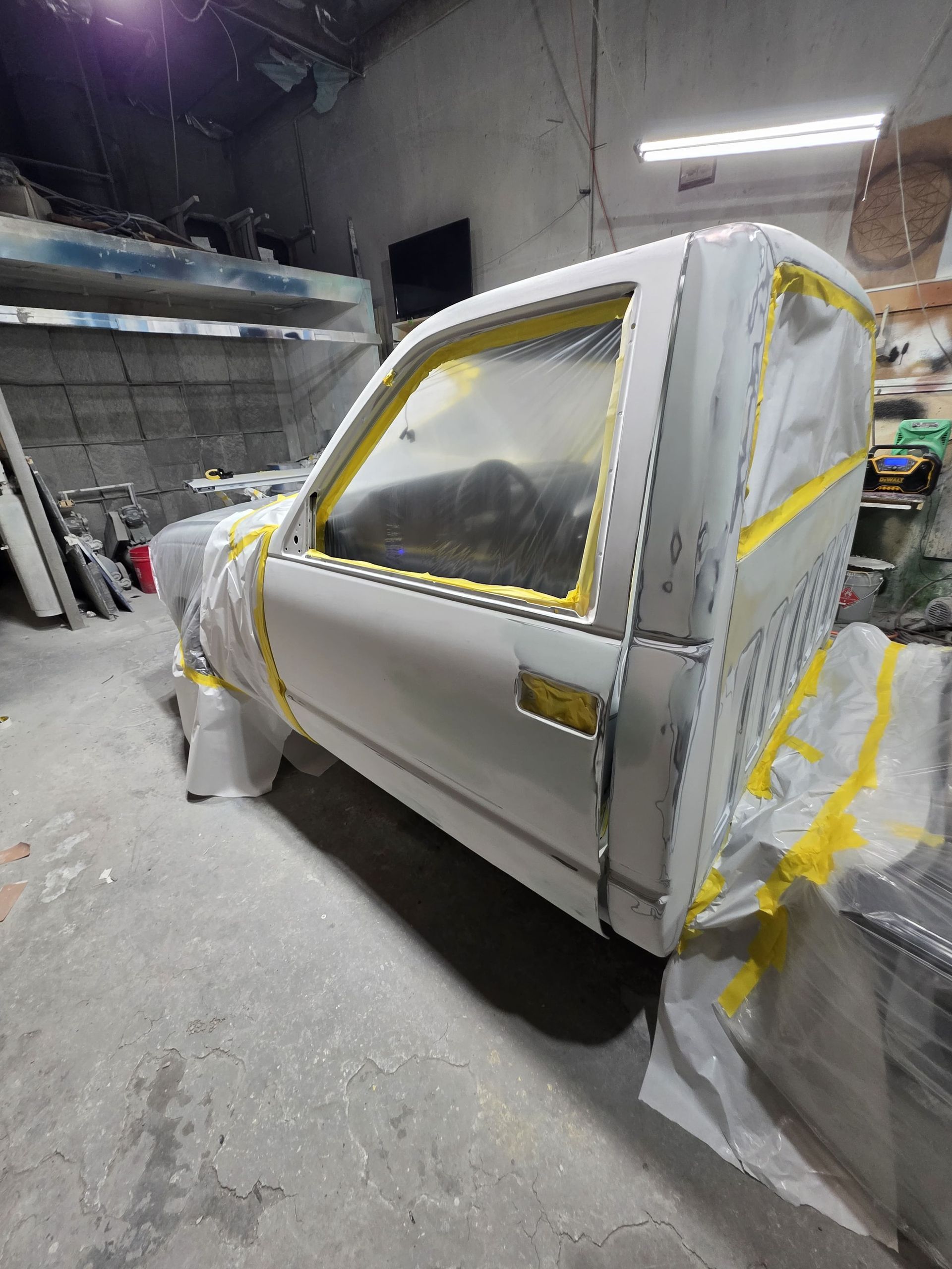 White car body in a paint booth, masked with yellow tape and plastic sheeting for painting