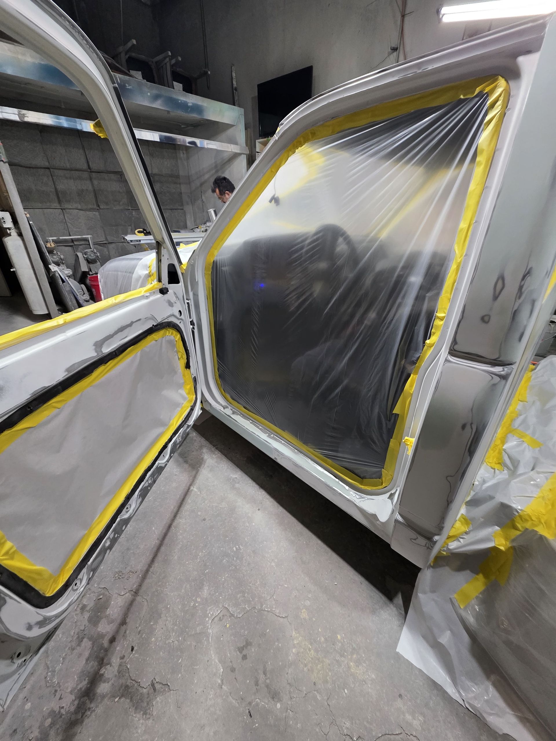 Two taped-off car doors in a workshop, covered in plastic and ready for painting