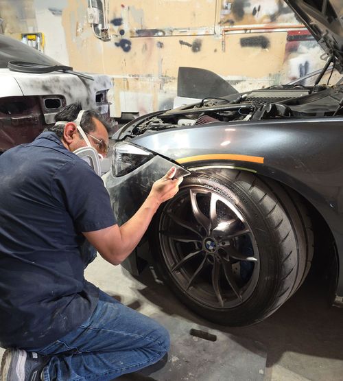 Mechanic painting the front fender of a black sports car in a garage