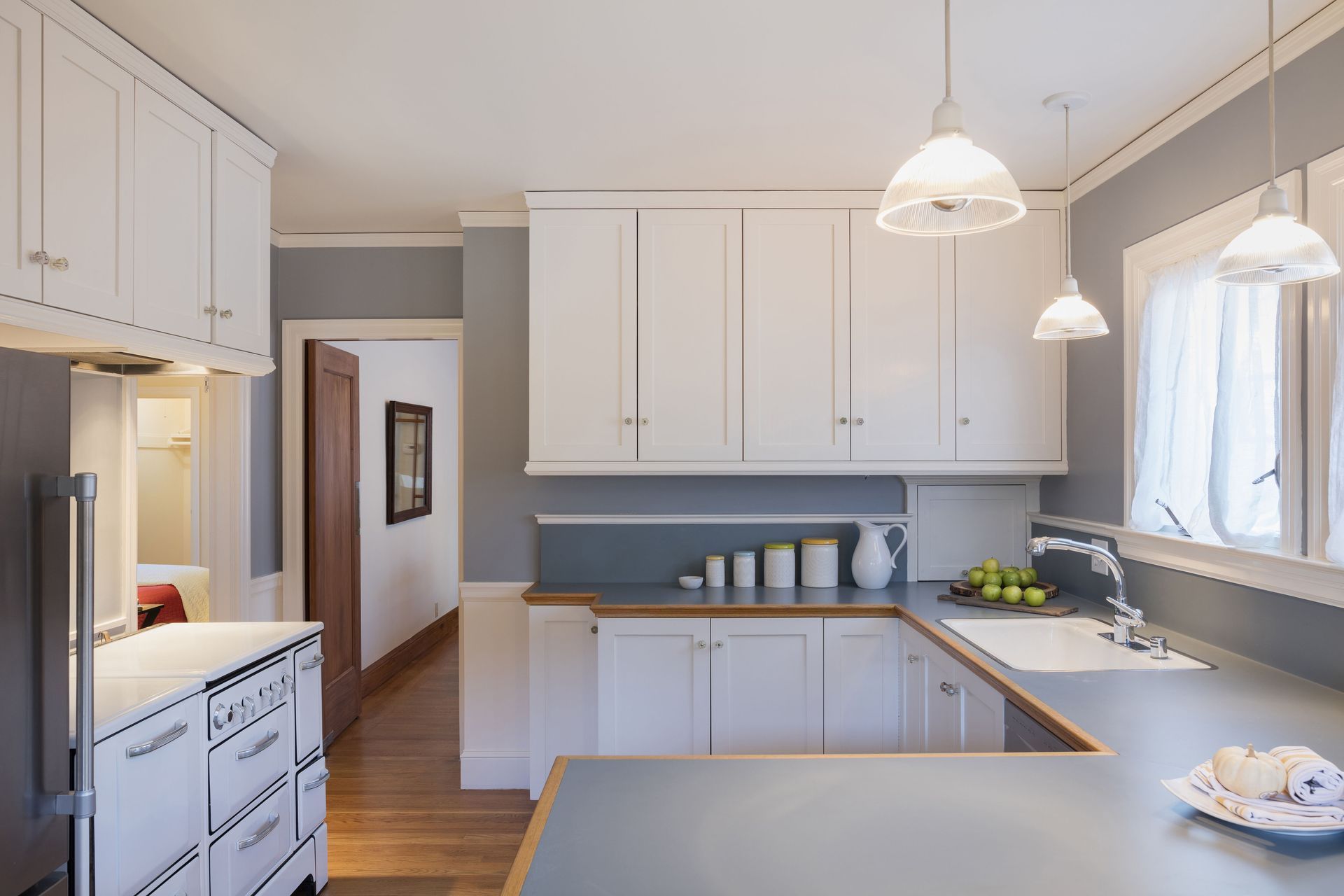 White cabinets in a light-filled kitchen with a u-shaped countertop, sink, and decorative pendant lights.