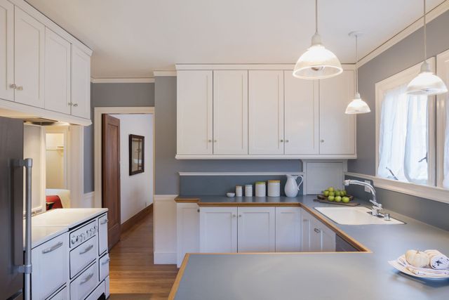 White cabinets in a light-filled kitchen with a u-shaped countertop, sink, and decorative pendant lights.