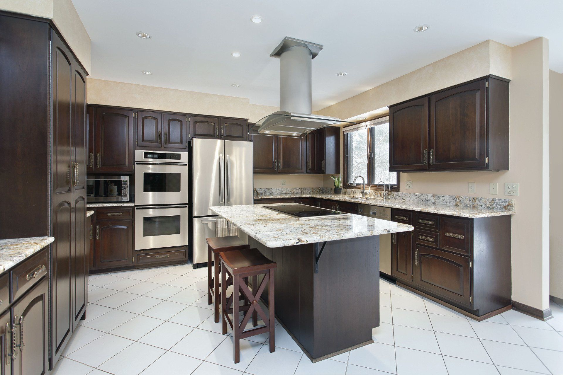 Dark wood kitchen with island, stainless steel appliances, and white tiled floor.