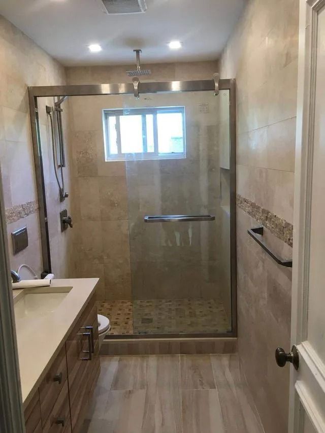 Bathroom with a glass shower, beige tiles, and a vanity with a sink.