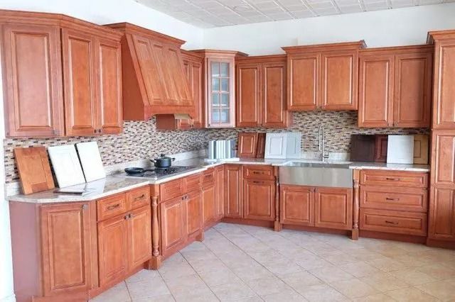 L-shaped kitchen with light brown wooden cabinets, stainless steel sink, and patterned backsplash.