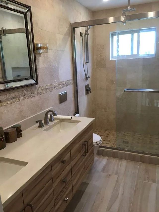 Bathroom with light wood vanity, glass shower, and beige tile.