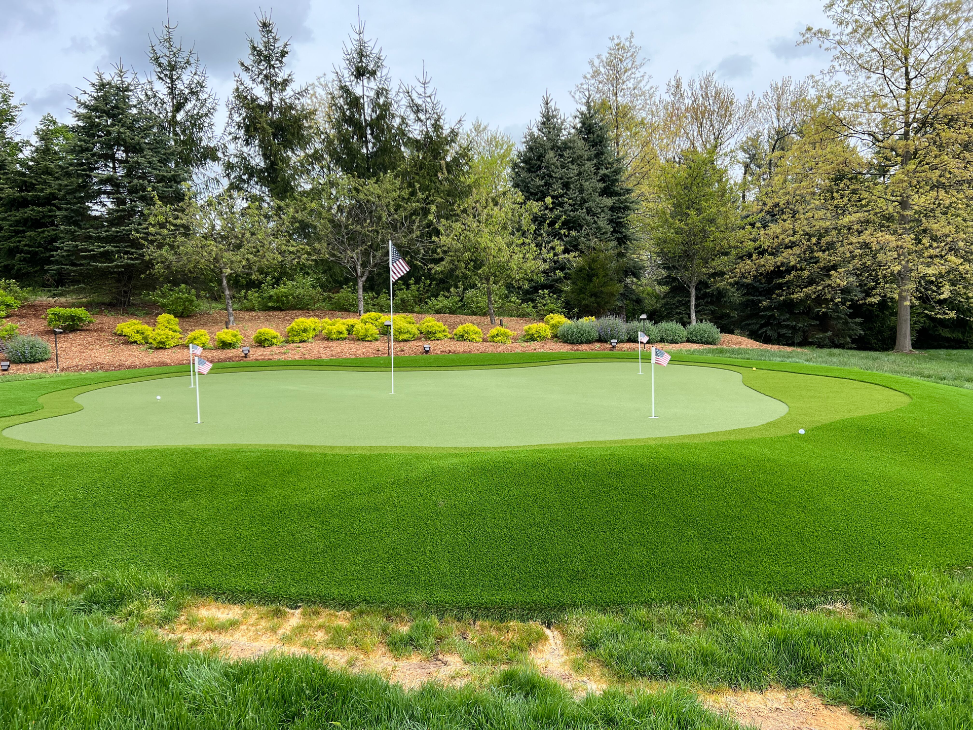 A golf course with a green and trees in the background.