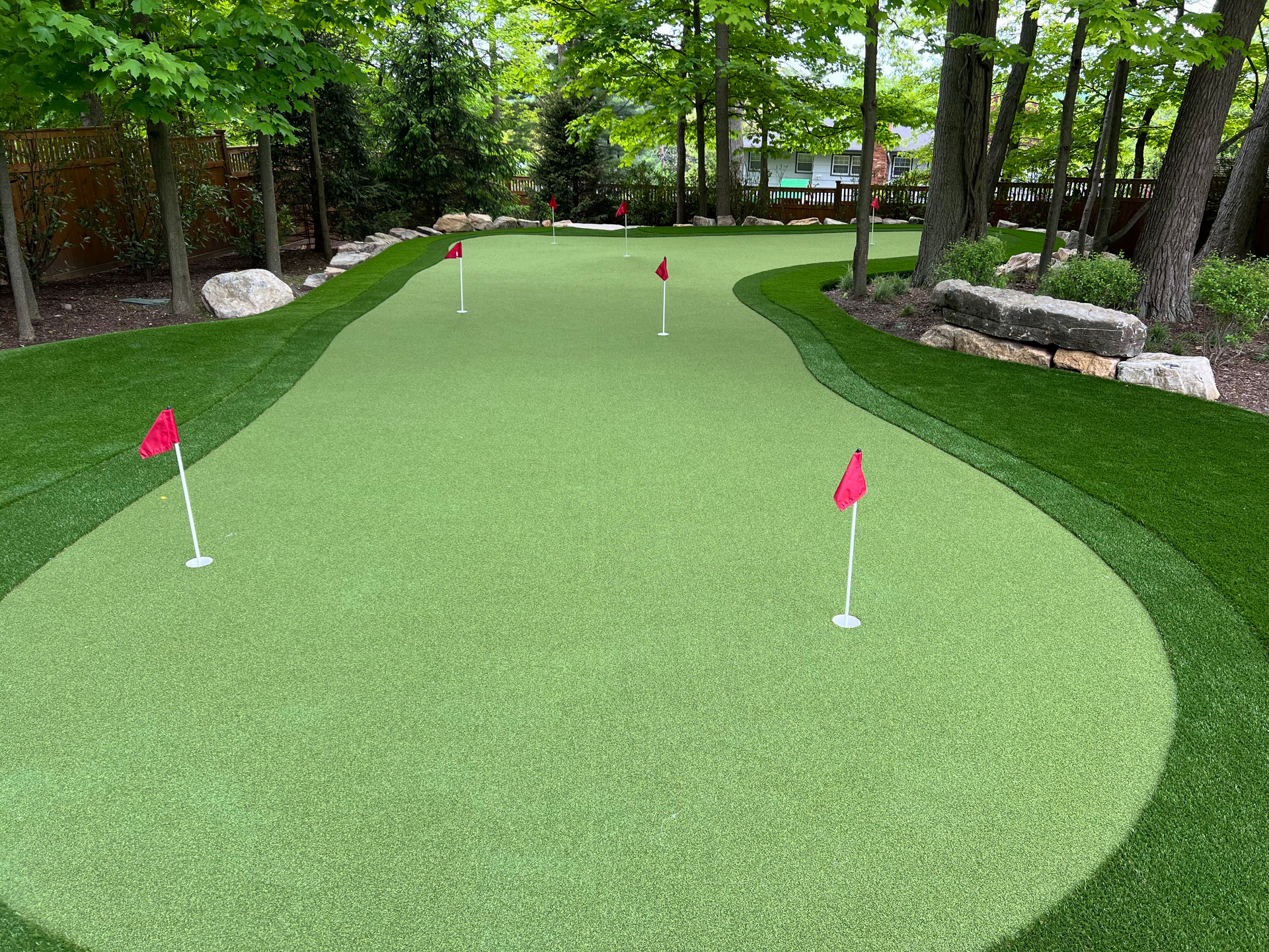 A green putting green with red flags and trees in the background.