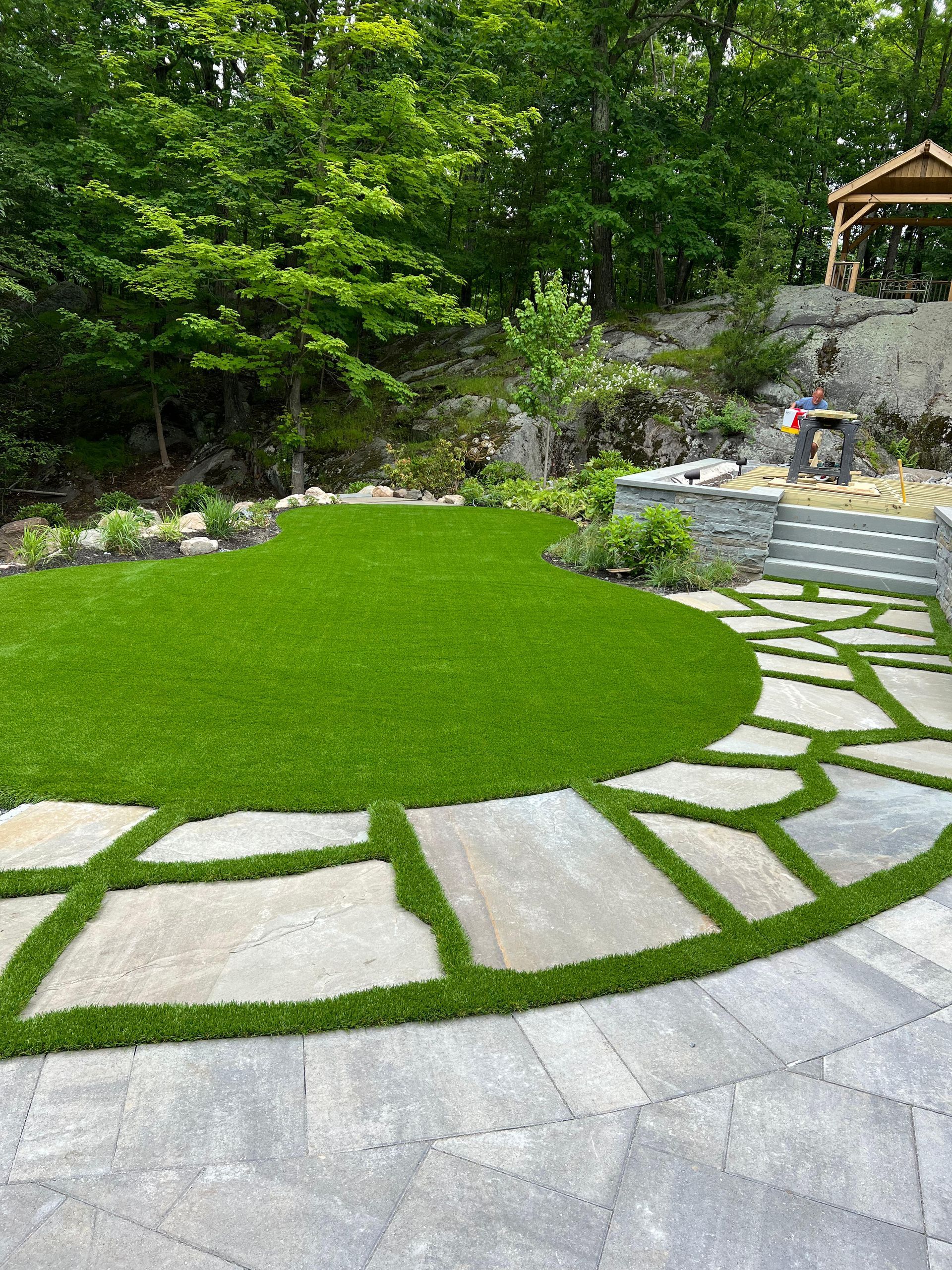 A stone walkway leading to a lush green lawn in a backyard.