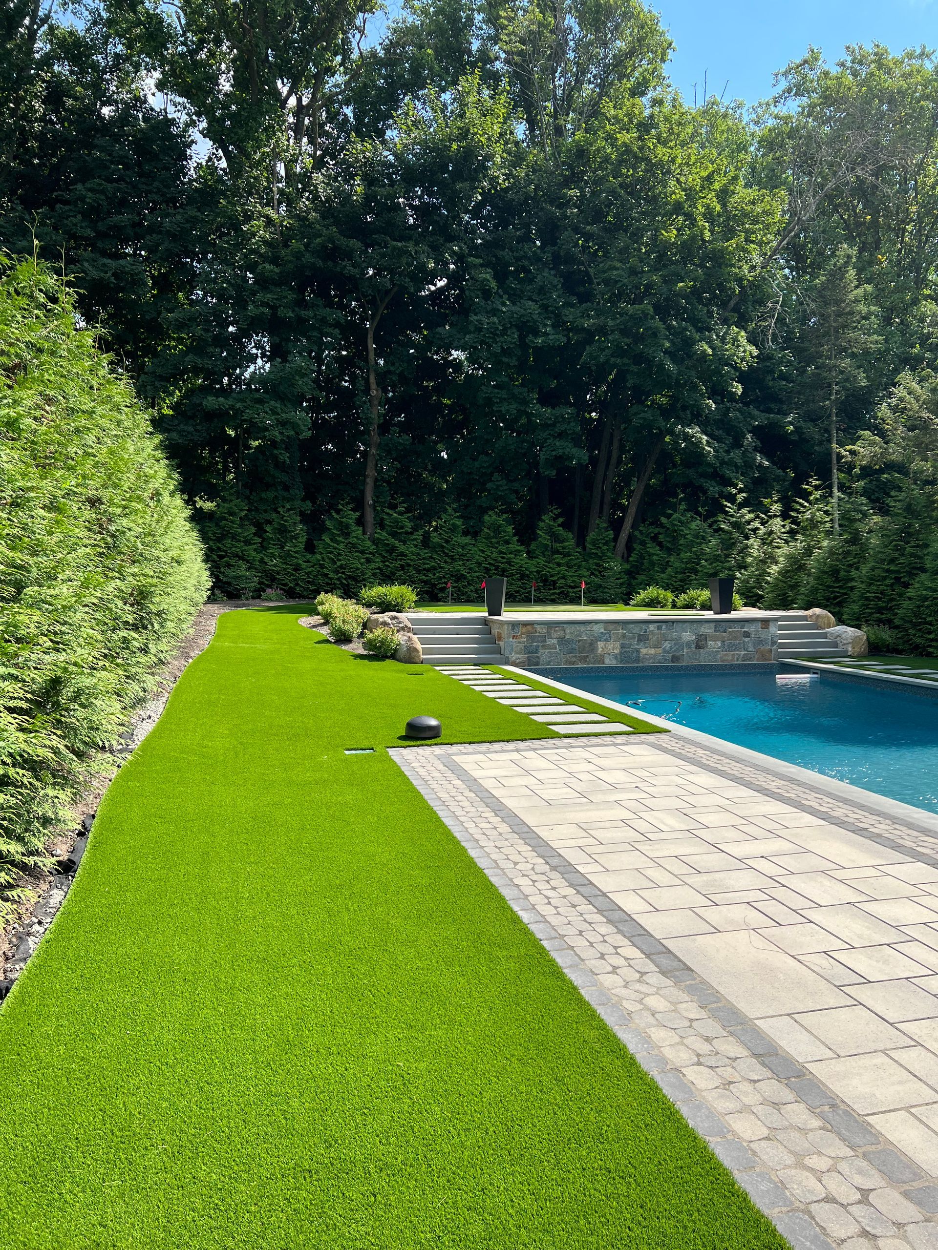 There is a swimming pool in the backyard with a lush green lawn.