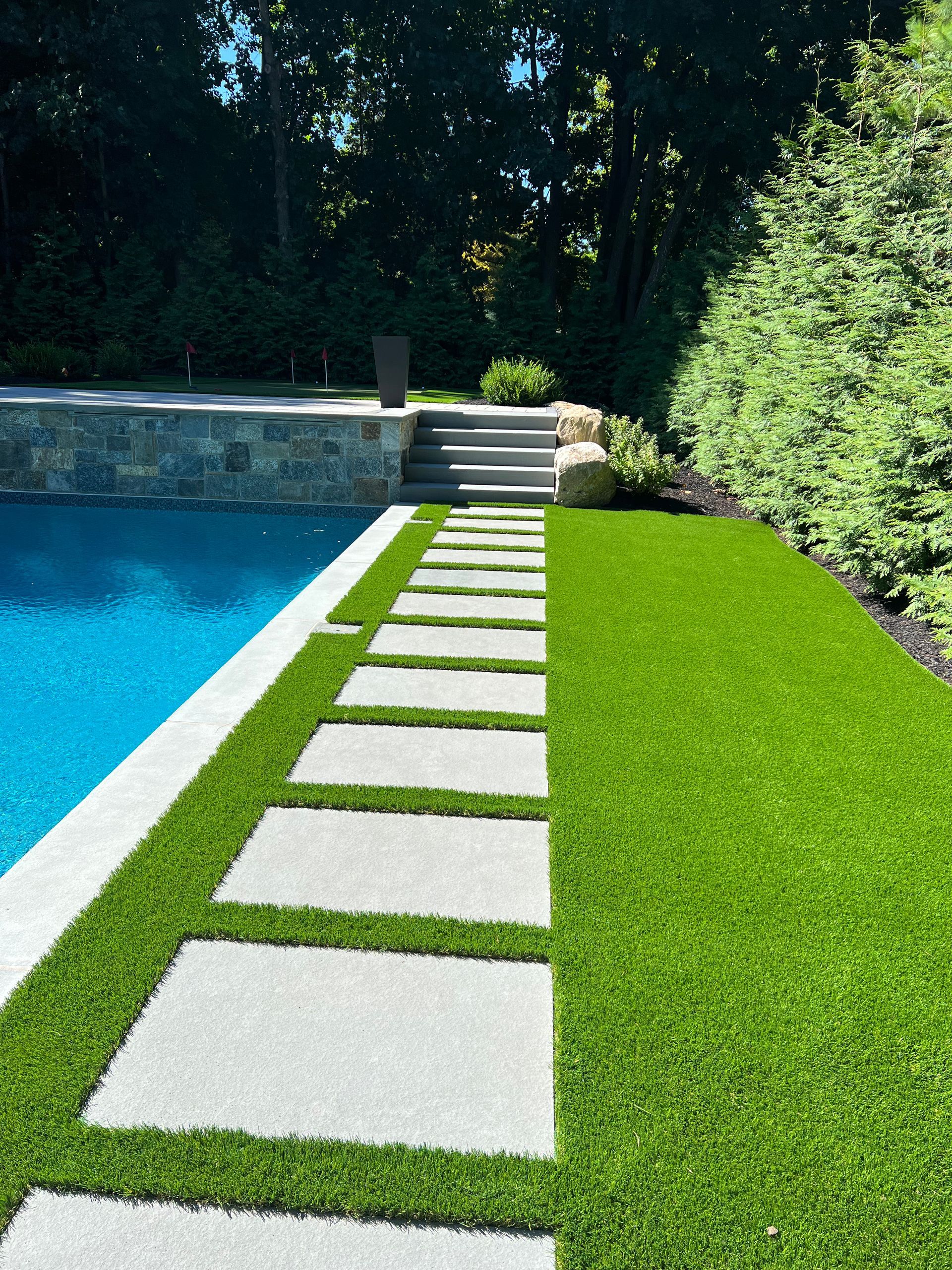 A lawn with a walkway leading to a swimming pool.