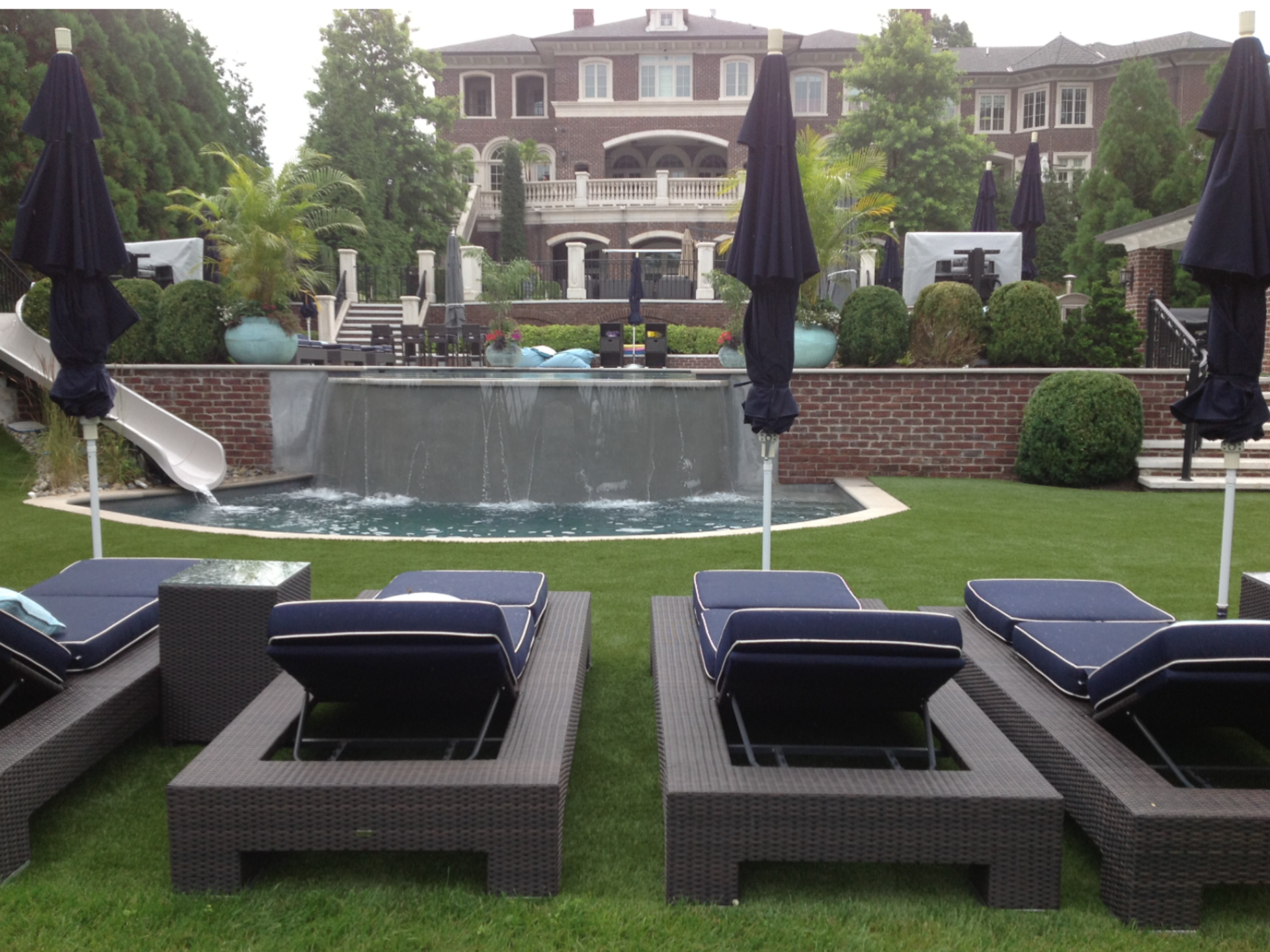 Lawn chairs and umbrellas in front of a large house.
