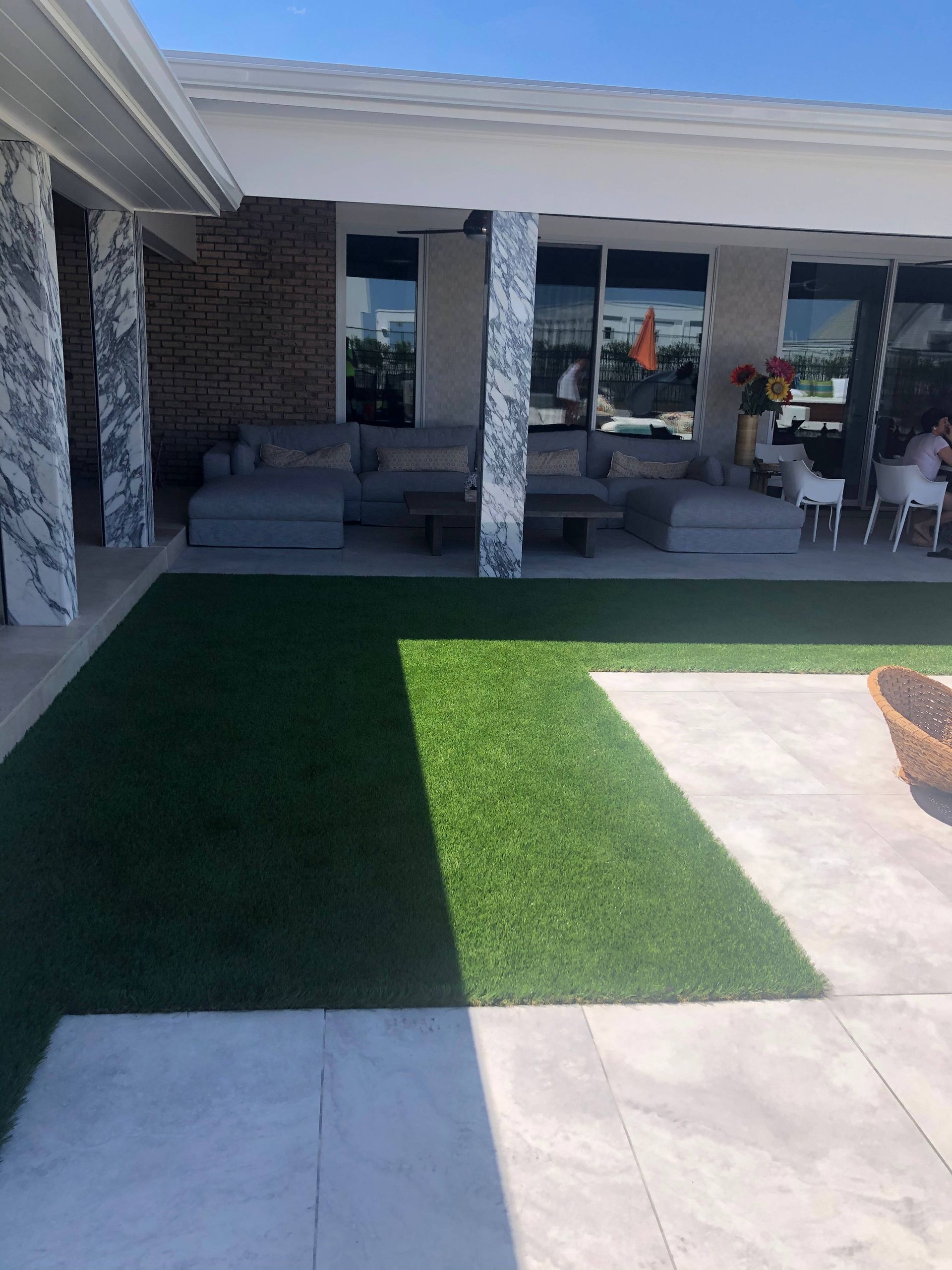 A patio with a lot of furniture and a lawn in front of a house.