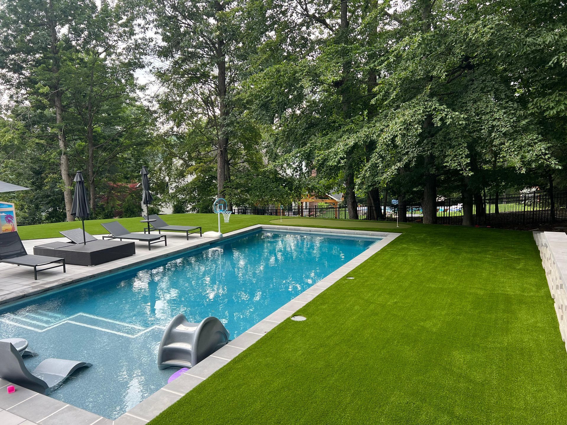 A large swimming pool surrounded by trees and grass in a backyard.
