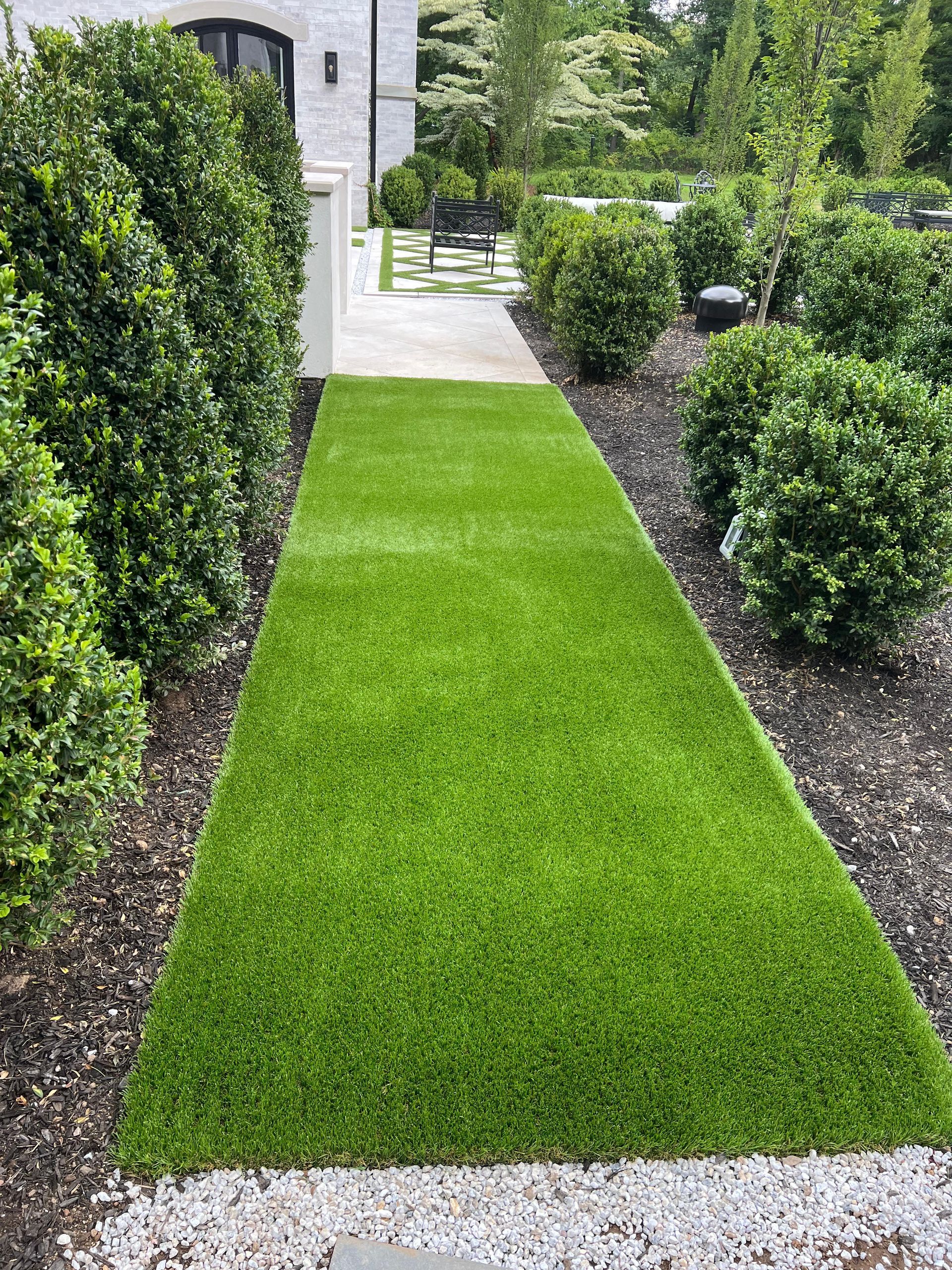 There is a long grassy path leading to a house.