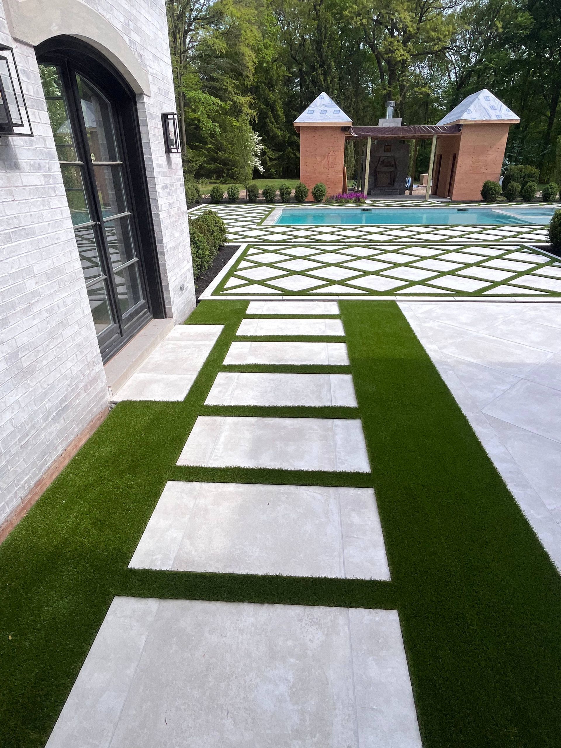A stone walkway leading to a swimming pool in a backyard.