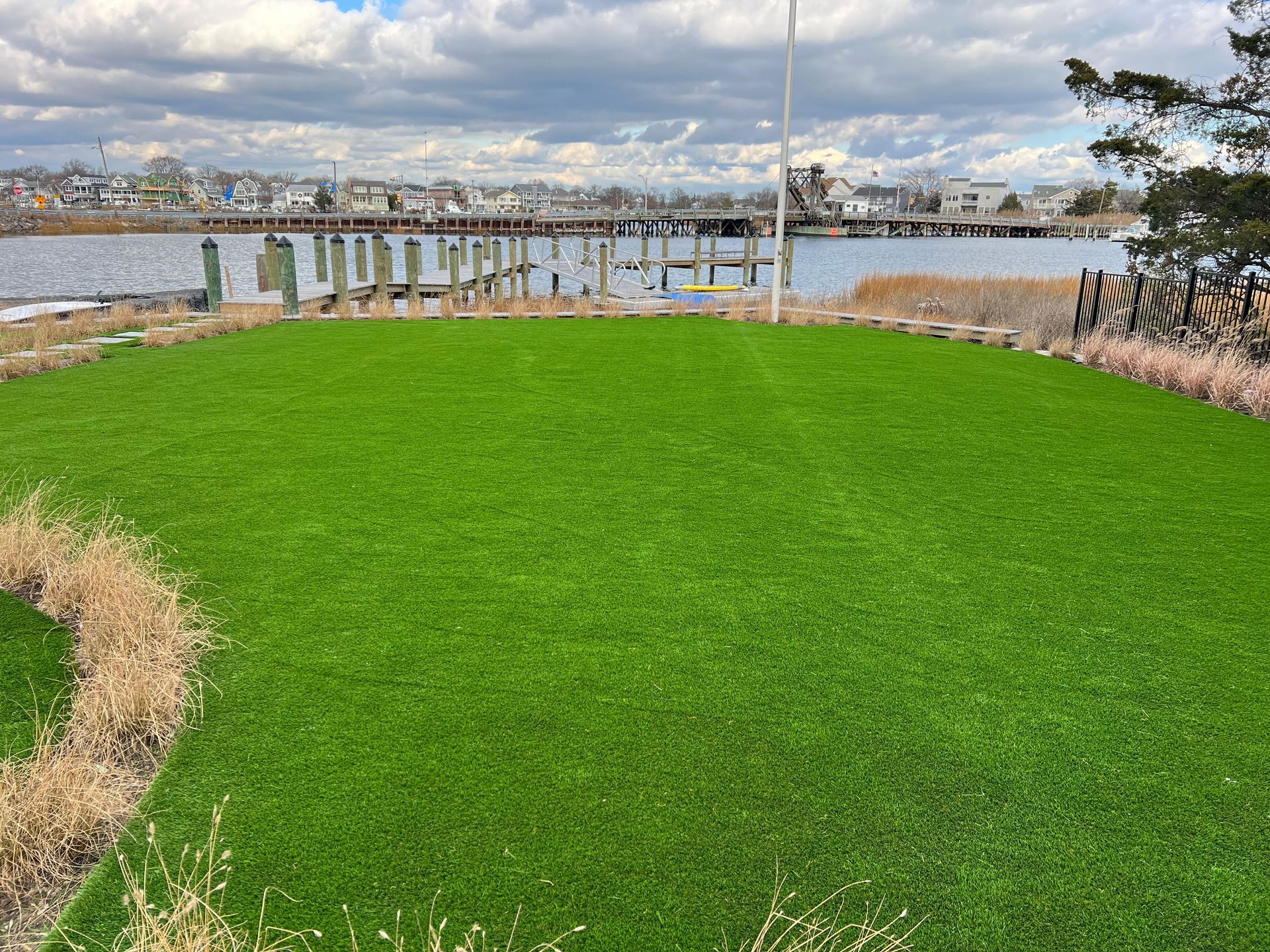 A lush green lawn next to a body of water with a dock in the background.