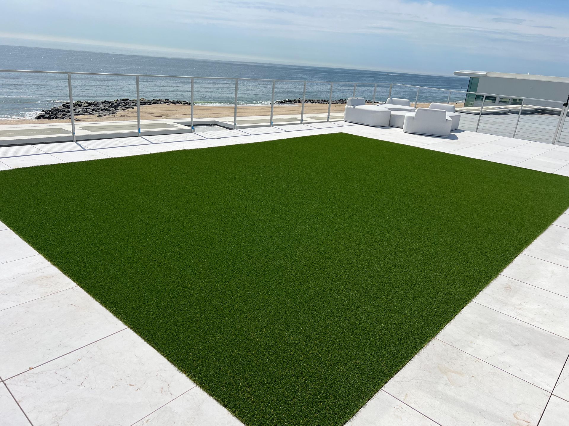 A large square of green grass on a patio with a view of the ocean.