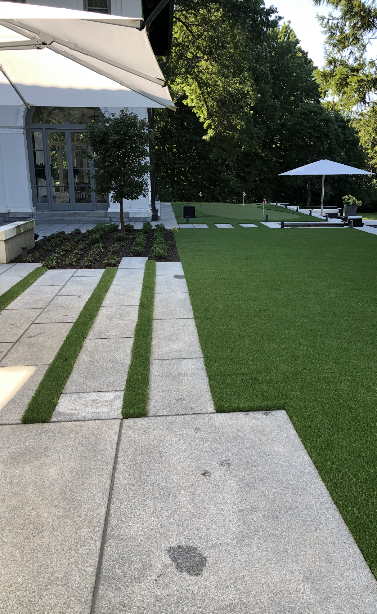 A walkway leading to a lush green lawn with a white umbrella in the background.