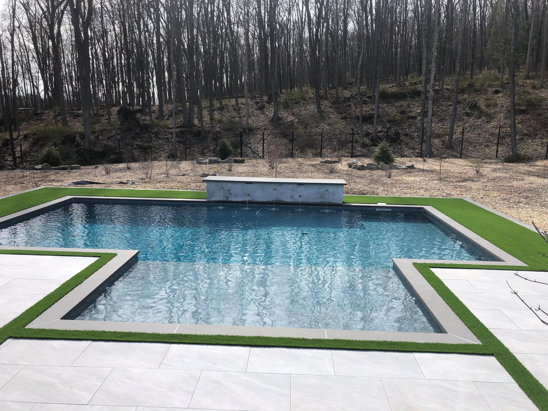 A large swimming pool surrounded by grass and trees in a backyard.