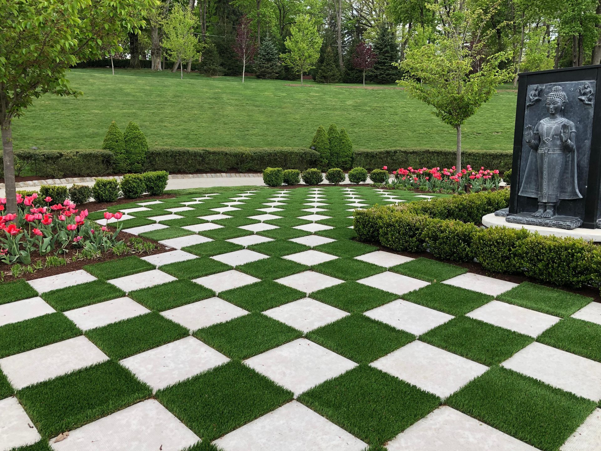 A lawn with a checkered pattern and a statue in the background.