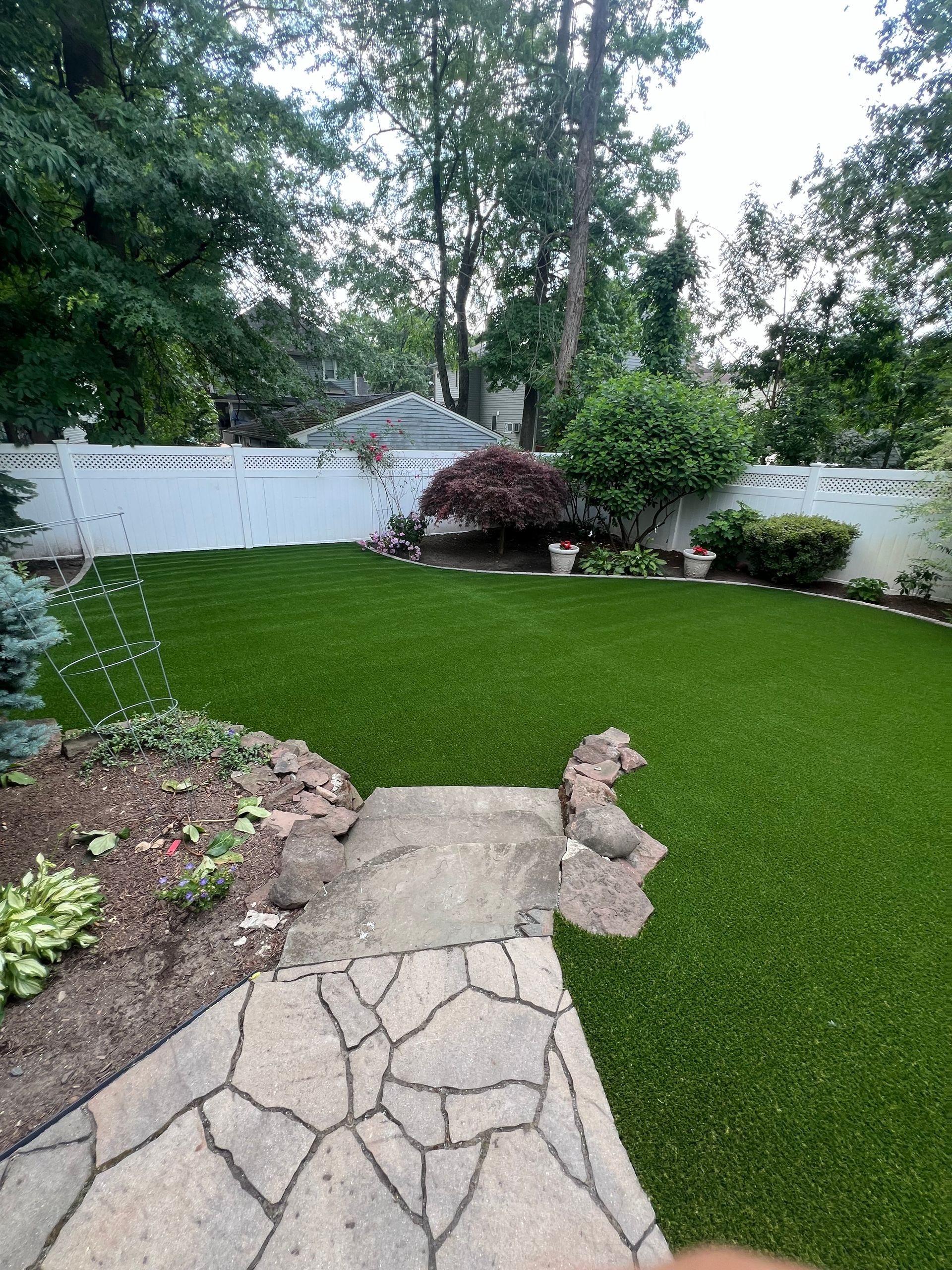 A backyard with a lush green lawn and a stone walkway.