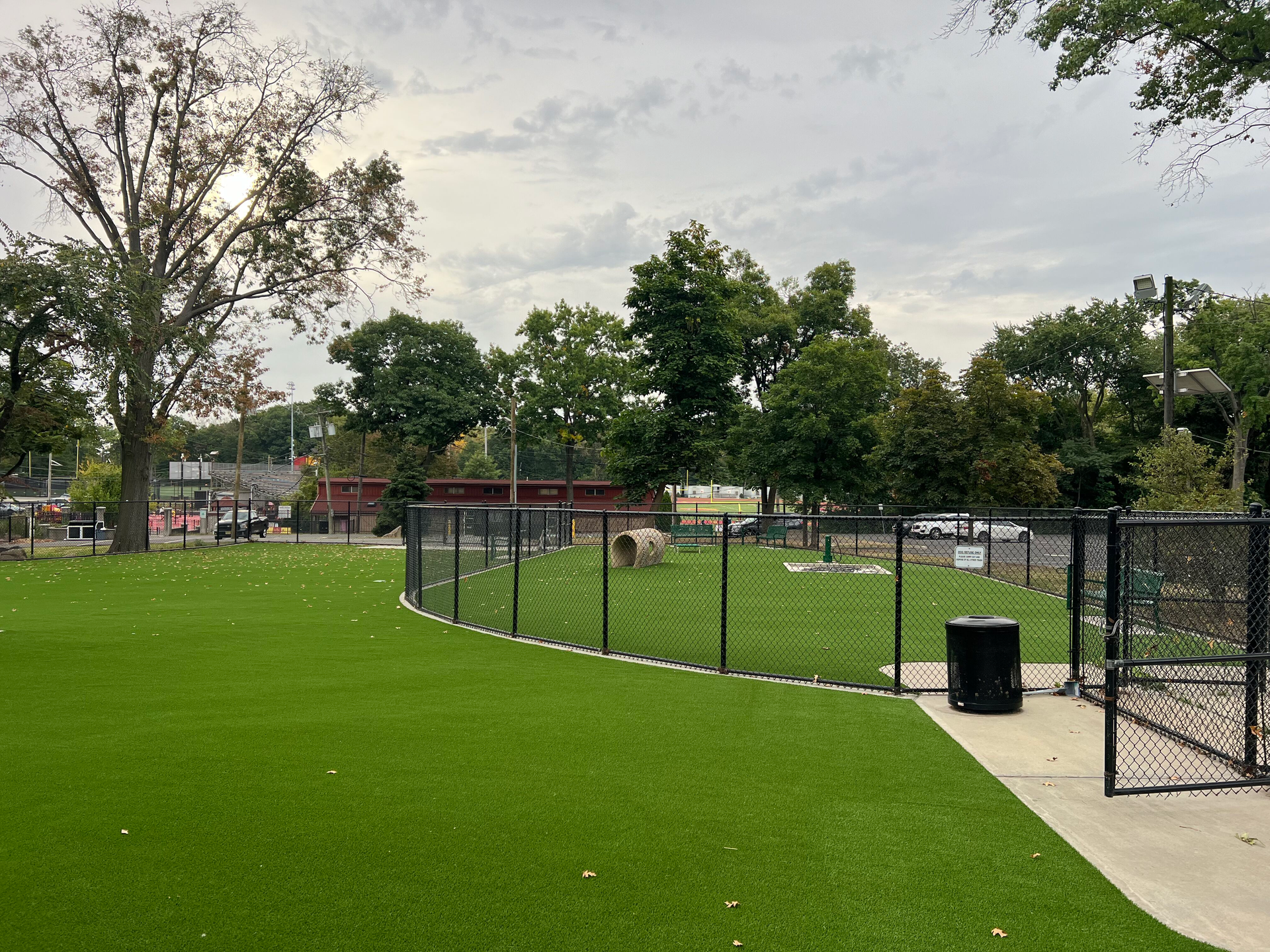 A dog park with a chain link fence and a trash can.
