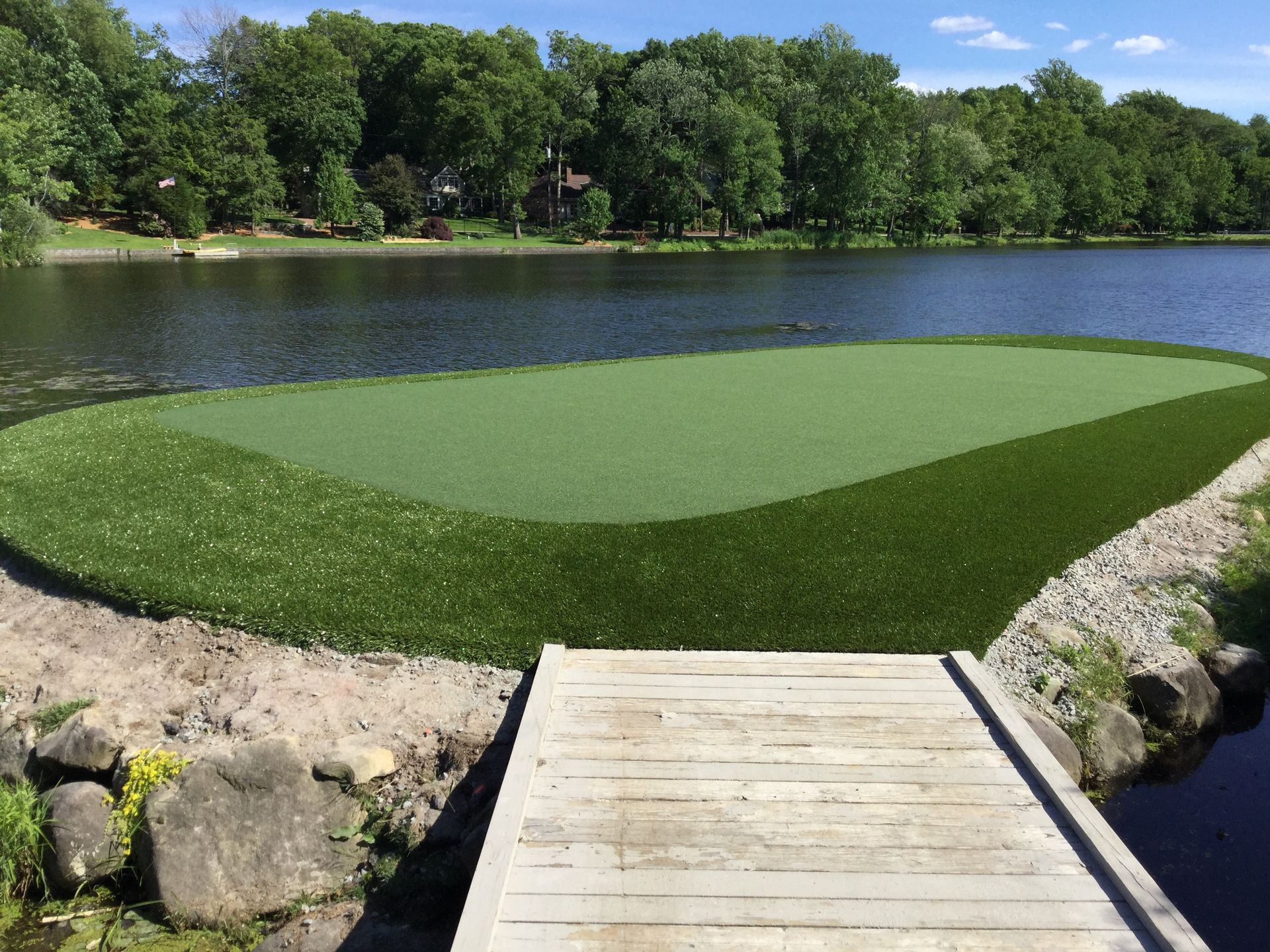 A wooden dock leads to a golf course next to a lake.