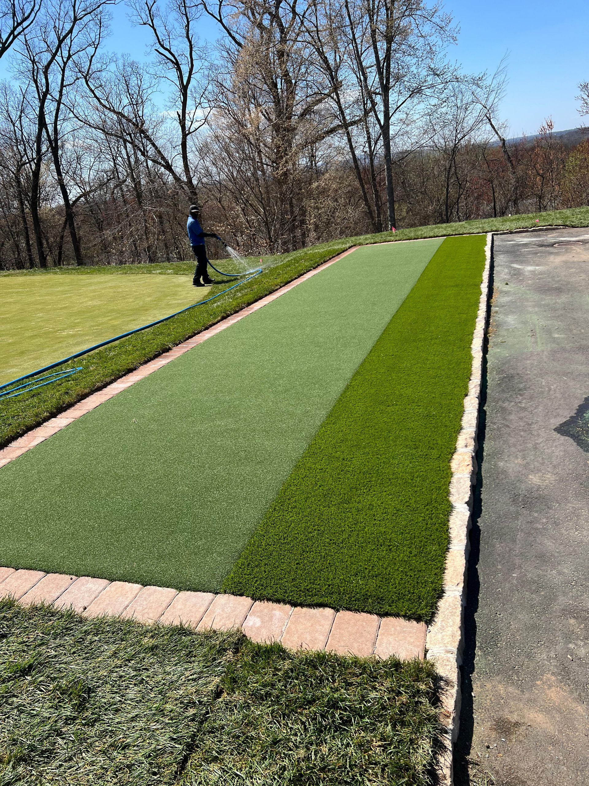 A man is watering a lawn with a hose.