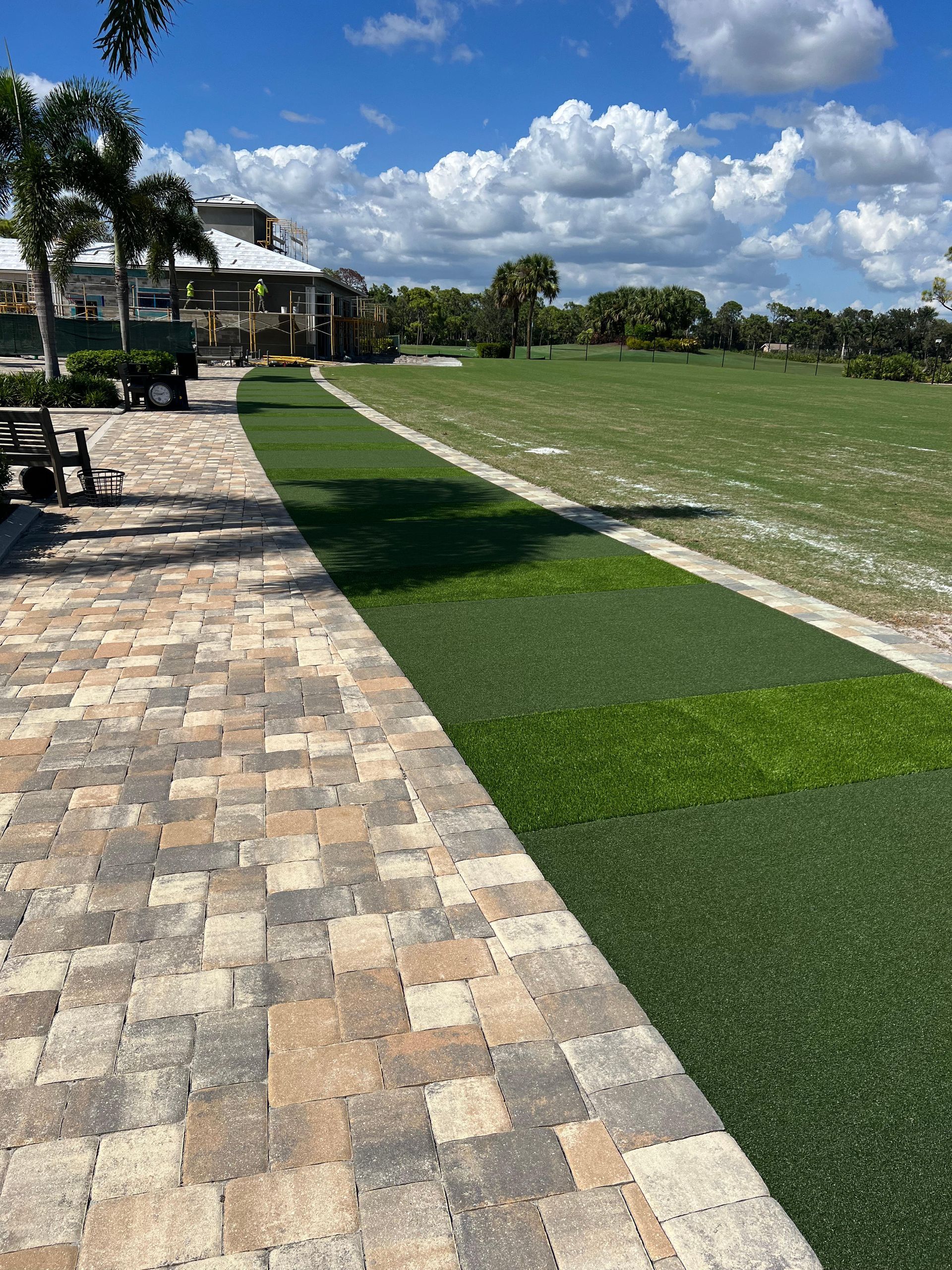 A brick walkway leading to a grassy field with a house in the background.